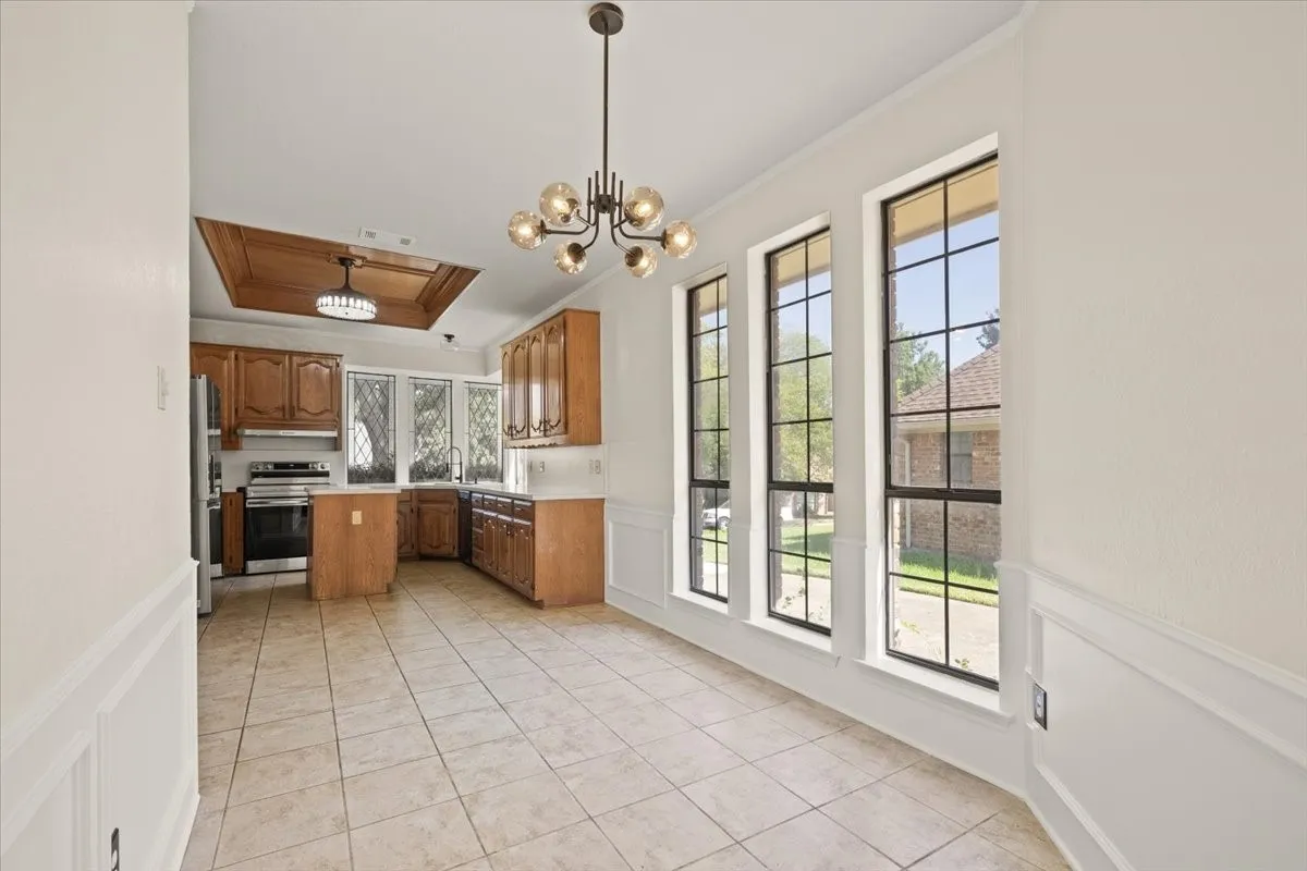 Tile flooring, white wainscoting, wood cabinetry, stainless steel appliances, and a coffered ceiling with recessed lighting