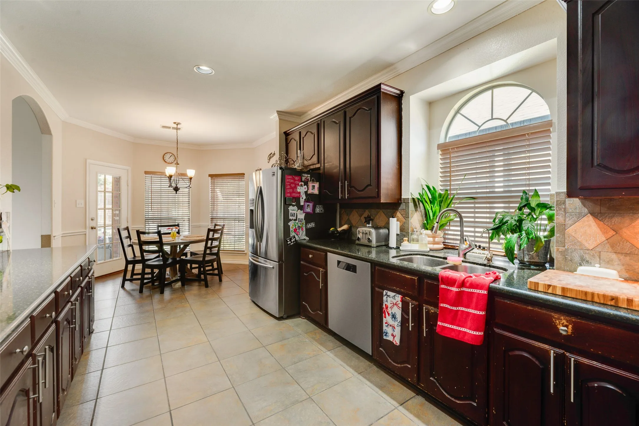Kitchen featuring dark wood cabinetry, stainless steel appliances, a tile backsplash, and a sink with a window overhead