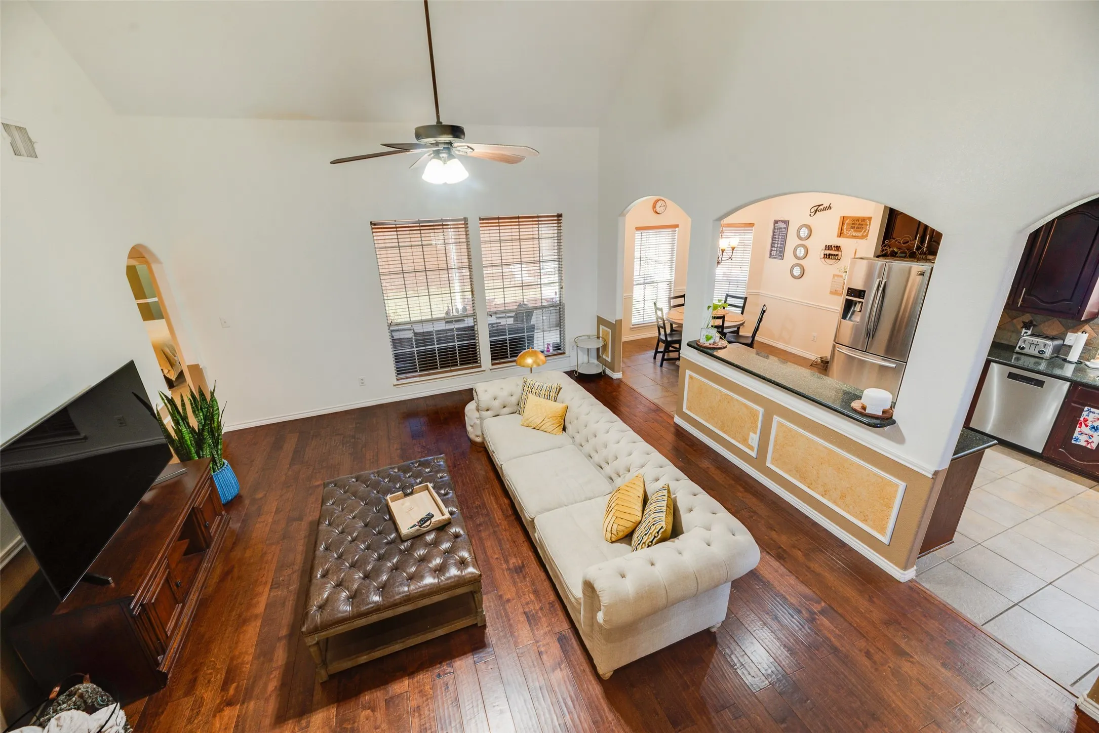 Vaulted ceiling with a ceiling fan, wood-finish flooring, arched doorways, and a kitchen pass-through with a breakfast bar