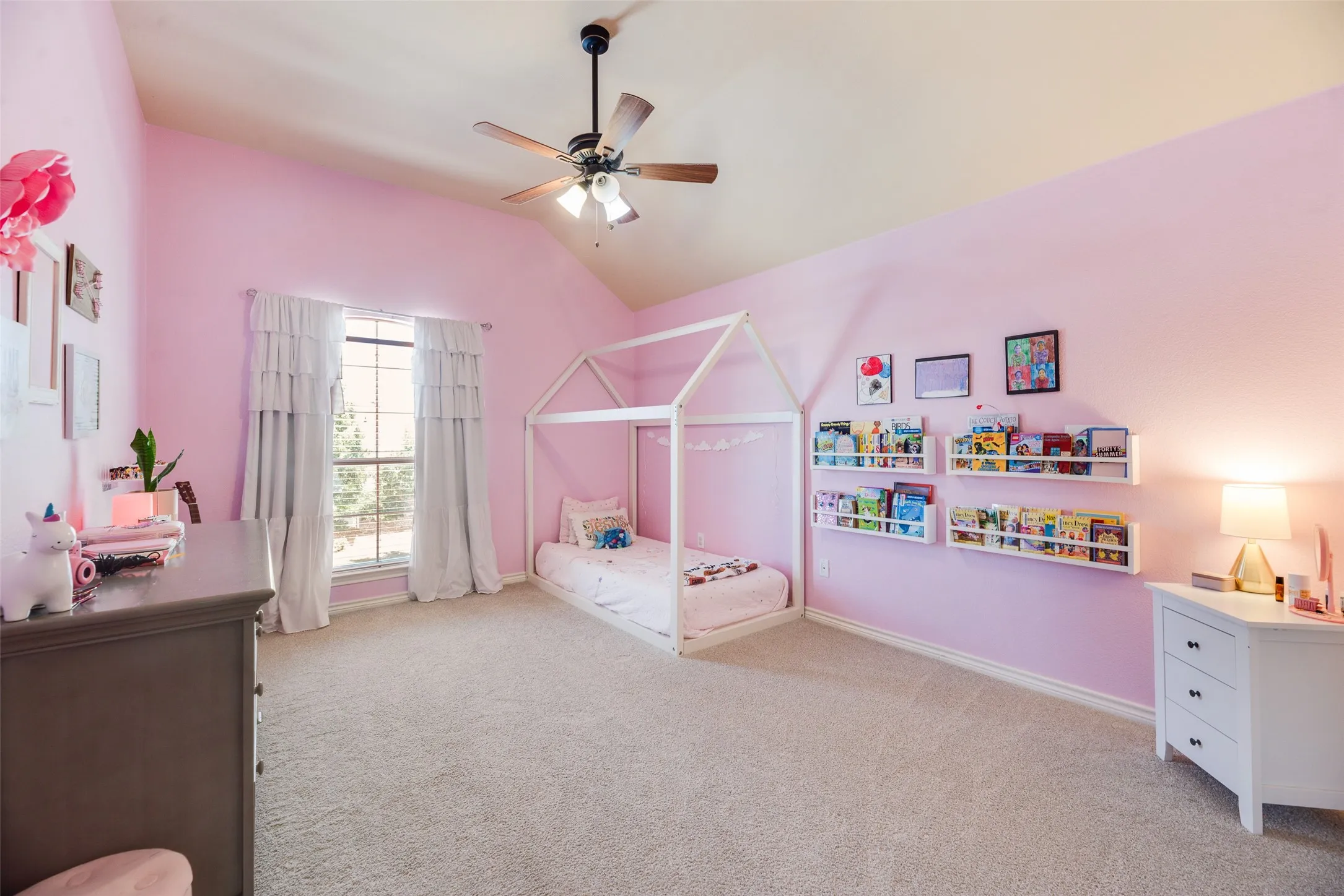 Bright, spacious bedroom featuring soft pink walls, carpeted flooring, and abundant natural light from a large multi-pane window with curtains
