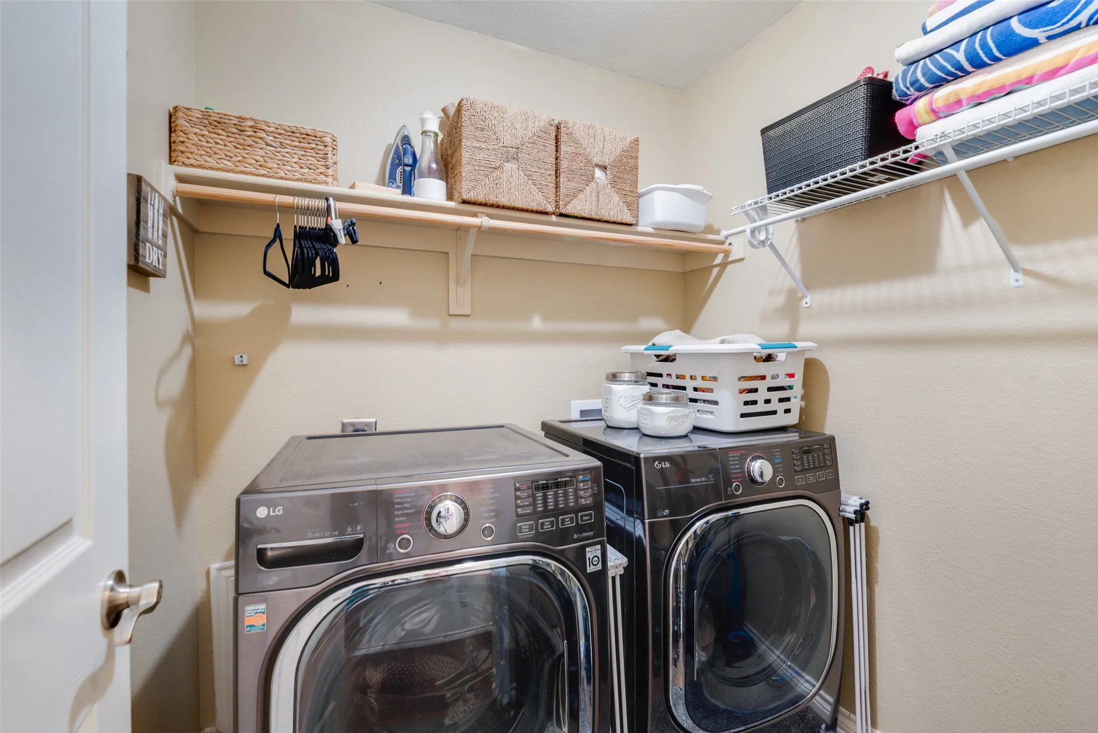 Laundry area featuring a wood-finish shelf, wall-mounted wire shelving, and a white interior door with a brushed nickel handle
