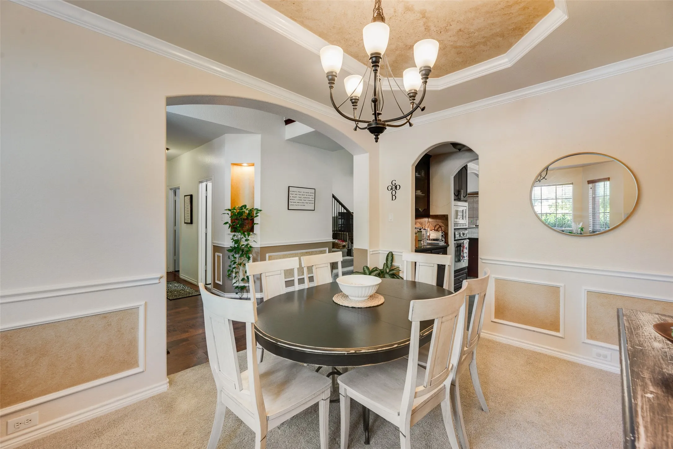 Tray ceiling with decorative finish and chandelier, arched doorways, wainscoting with decorative panels, and wall-to-wall carpeting