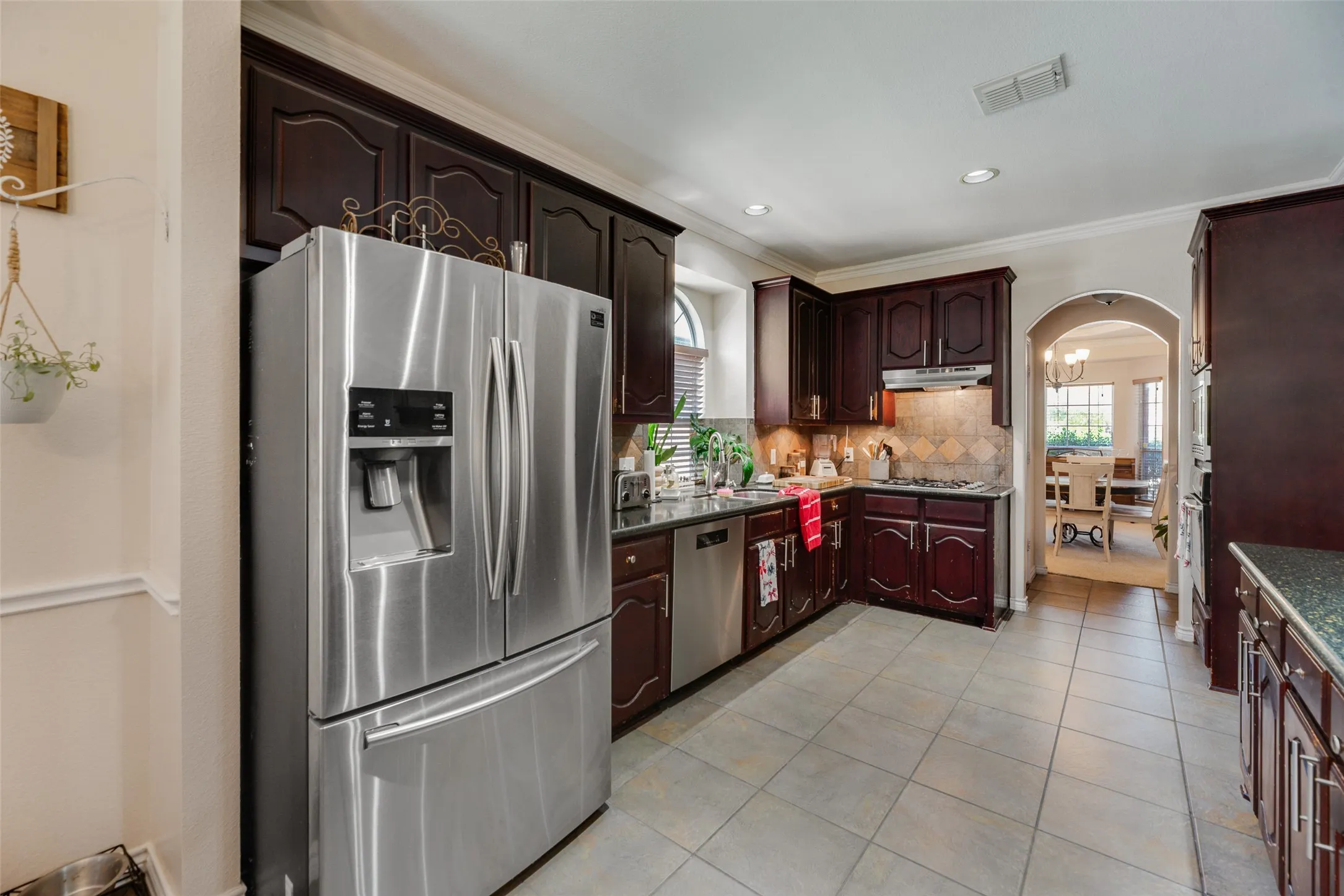 Kitchen featuring dark wood cabinetry, stainless steel appliances, tile flooring, and an arched doorway