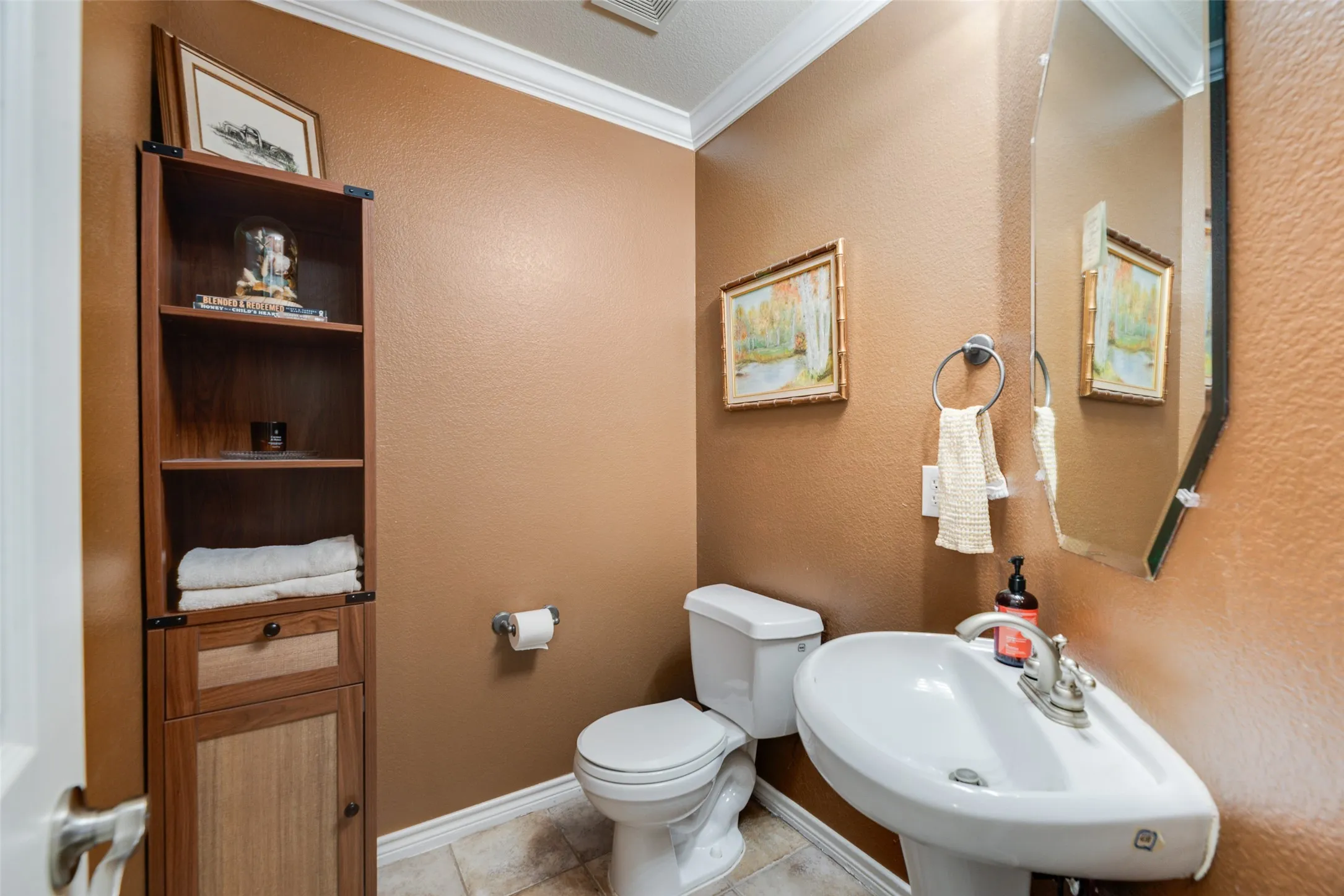 Pedestal sink with chrome faucet, toilet, and built-in wood-finish shelving with a lower cabinet