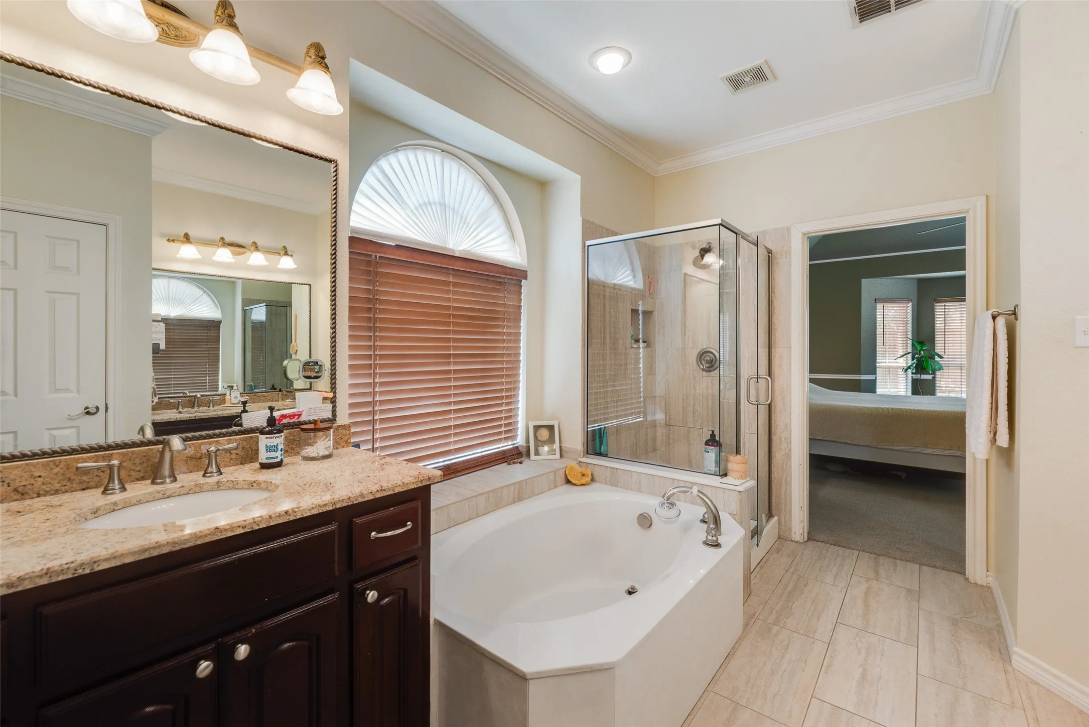 Corner soaking tub with integrated deck, glass-enclosed shower, and a single vanity featuring a granite countertop