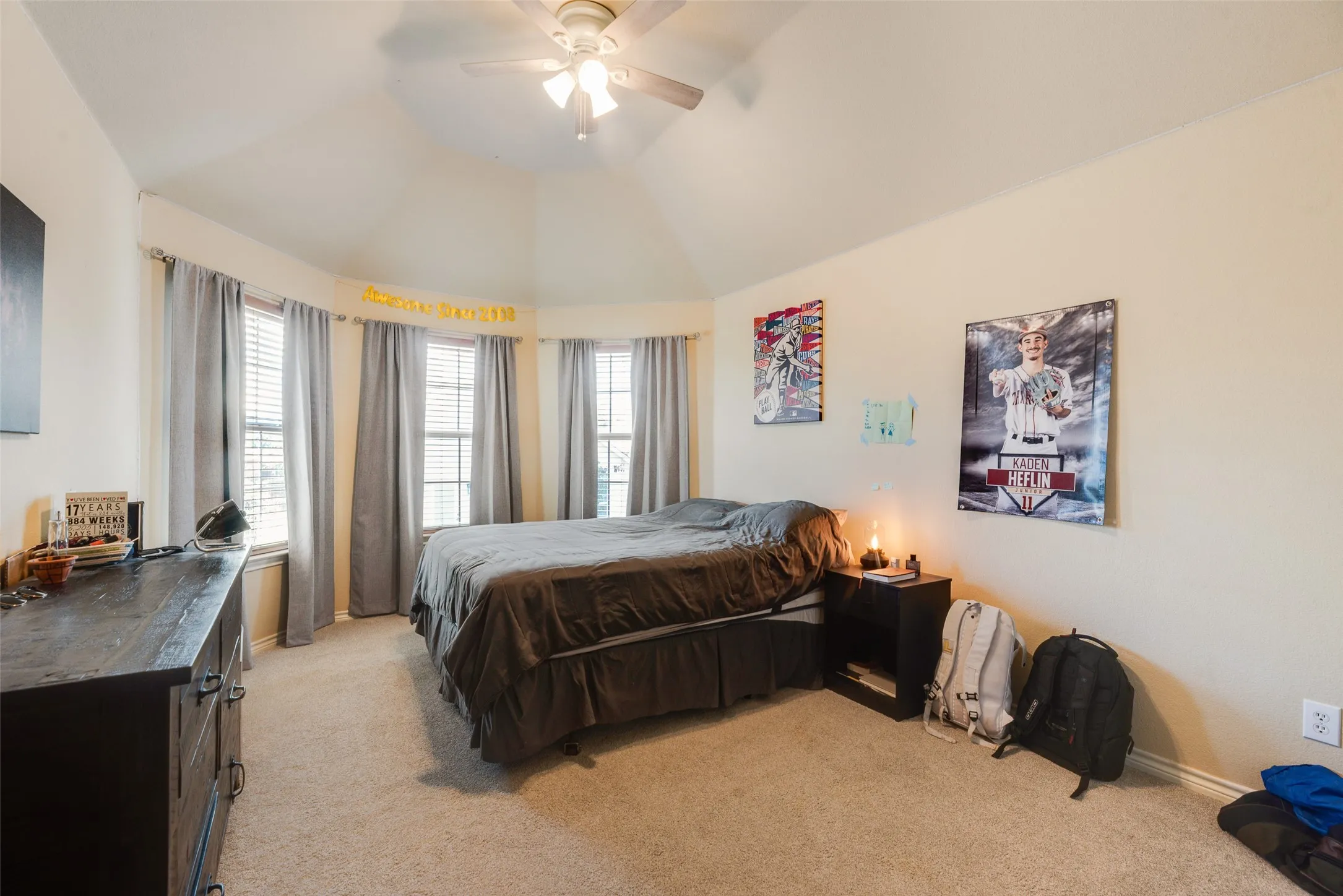 Vaulted ceiling with a ceiling fan, carpeted flooring, and a bay window configuration