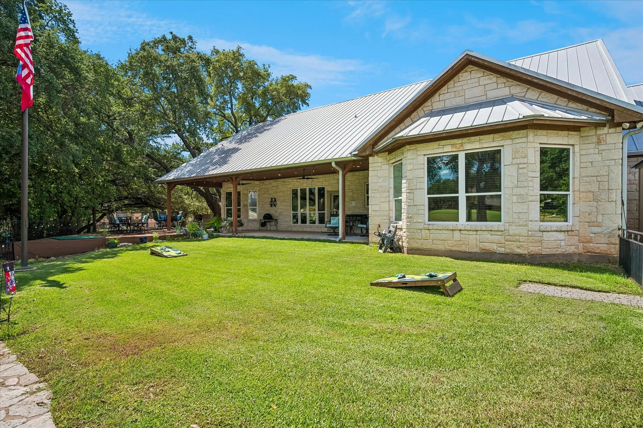 Stone exterior with a metal roof, featuring a covered patio, multiple windows, and a manicured lawn