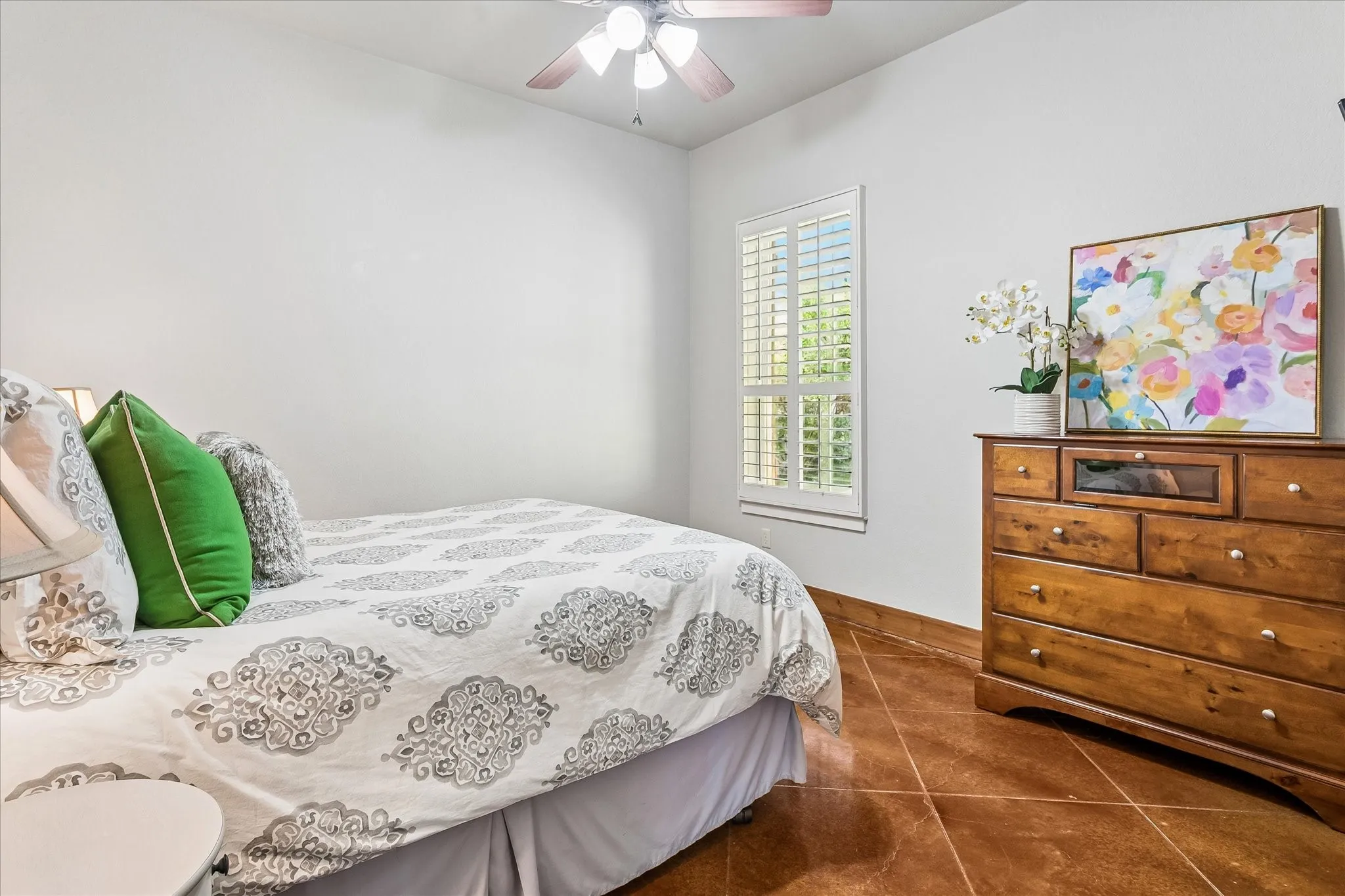 Tile flooring, window with plantation shutters, ceiling fan, white walls, and wood trim