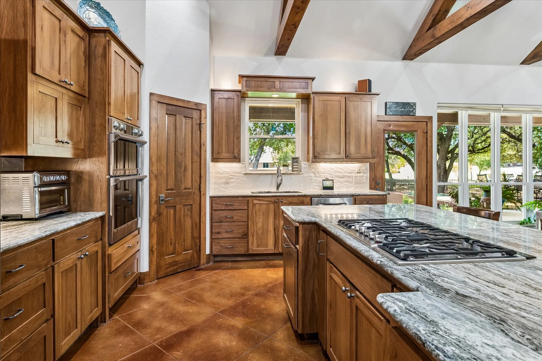 Kitchen featuring vaulted ceilings with exposed wood beams, wood-finish cabinetry, built-in double ovens, and an island with a gas cooktop