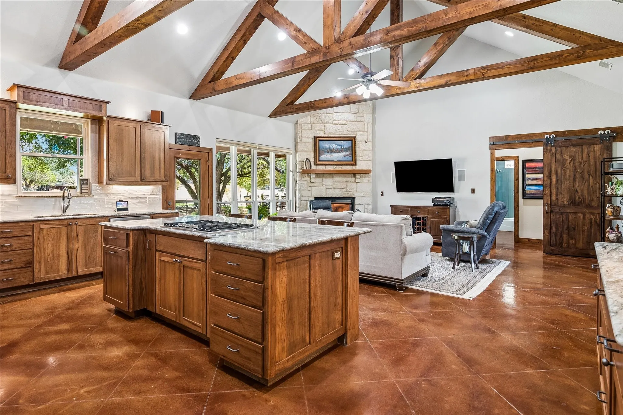 Vaulted ceiling with exposed wood beams, stone fireplace, wood-finish flooring, custom wood cabinetry, and a sliding barn door