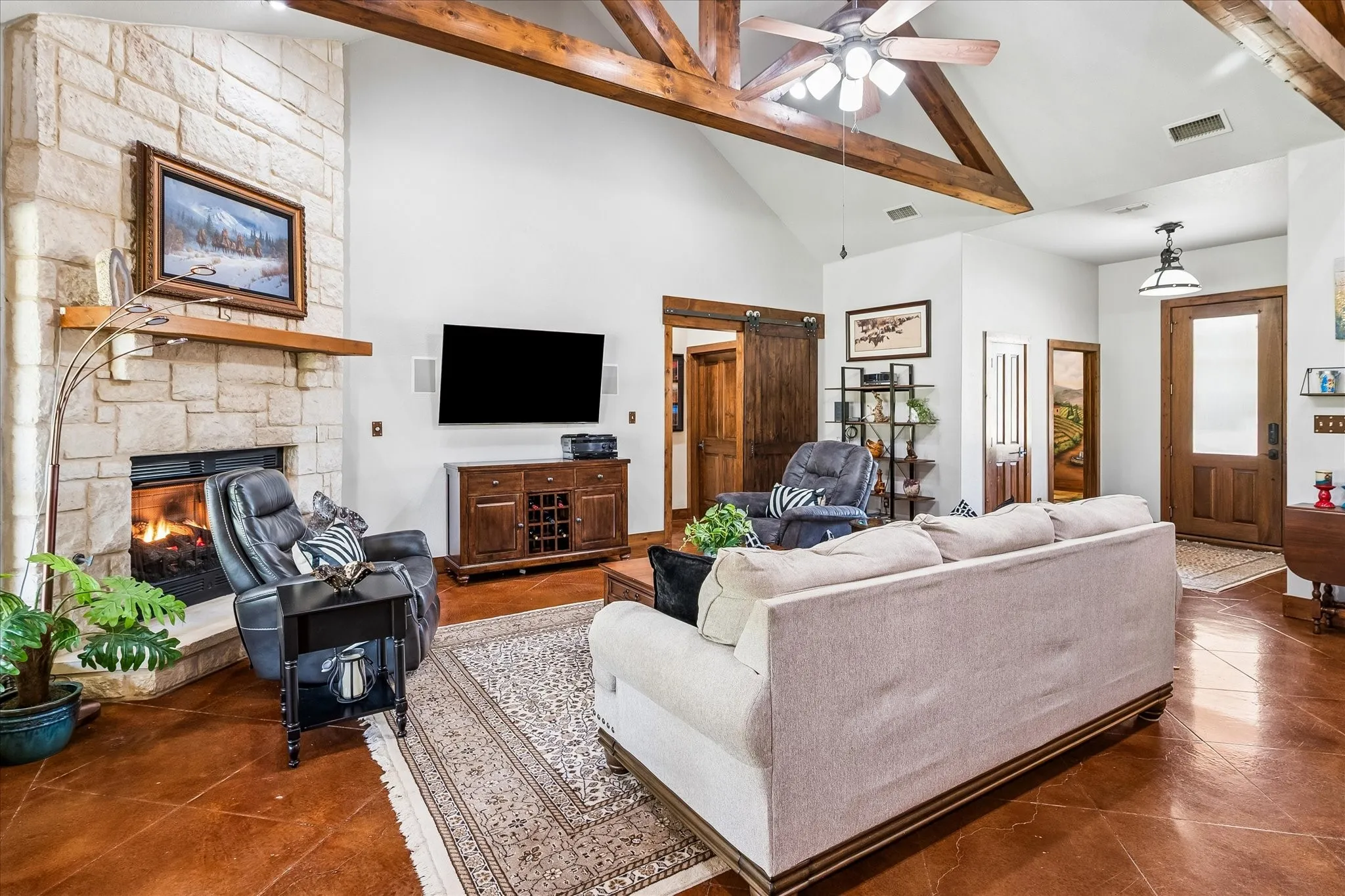 Vaulted ceiling with exposed wood beams, stone fireplace with wood mantel, wood-finish flooring, and a barn door entry