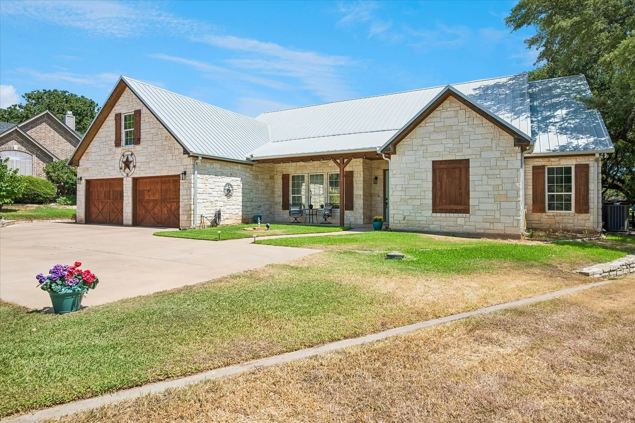 Stone exterior with a metal roof, a two-car garage with wood-finish doors, and a covered porch with timber posts