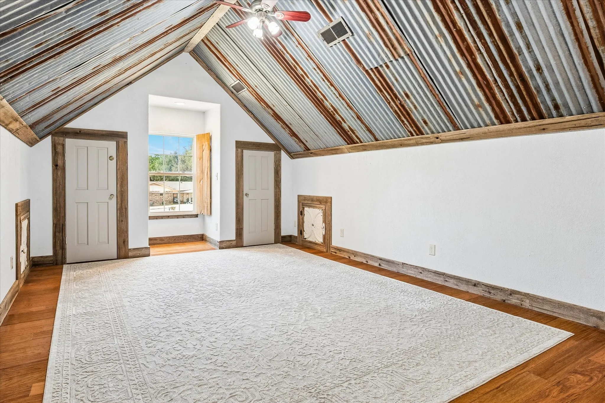 Vaulted corrugated metal ceiling, wood-finish flooring, white paneled doors, and wooden window shutters