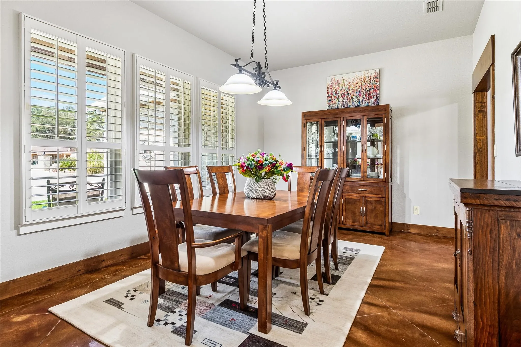 Dining area with multiple windows featuring plantation shutters, warm-toned flooring, and a built-in display cabinet