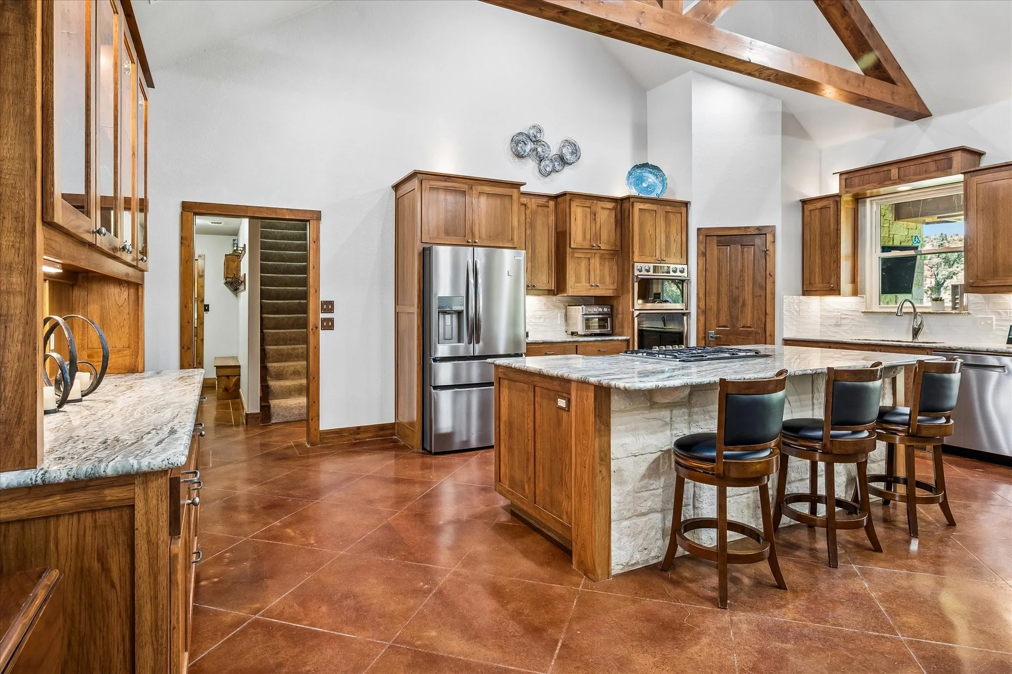 Kitchen featuring a large island with stone base, stainless steel appliances, wood cabinetry, and exposed wood ceiling beams