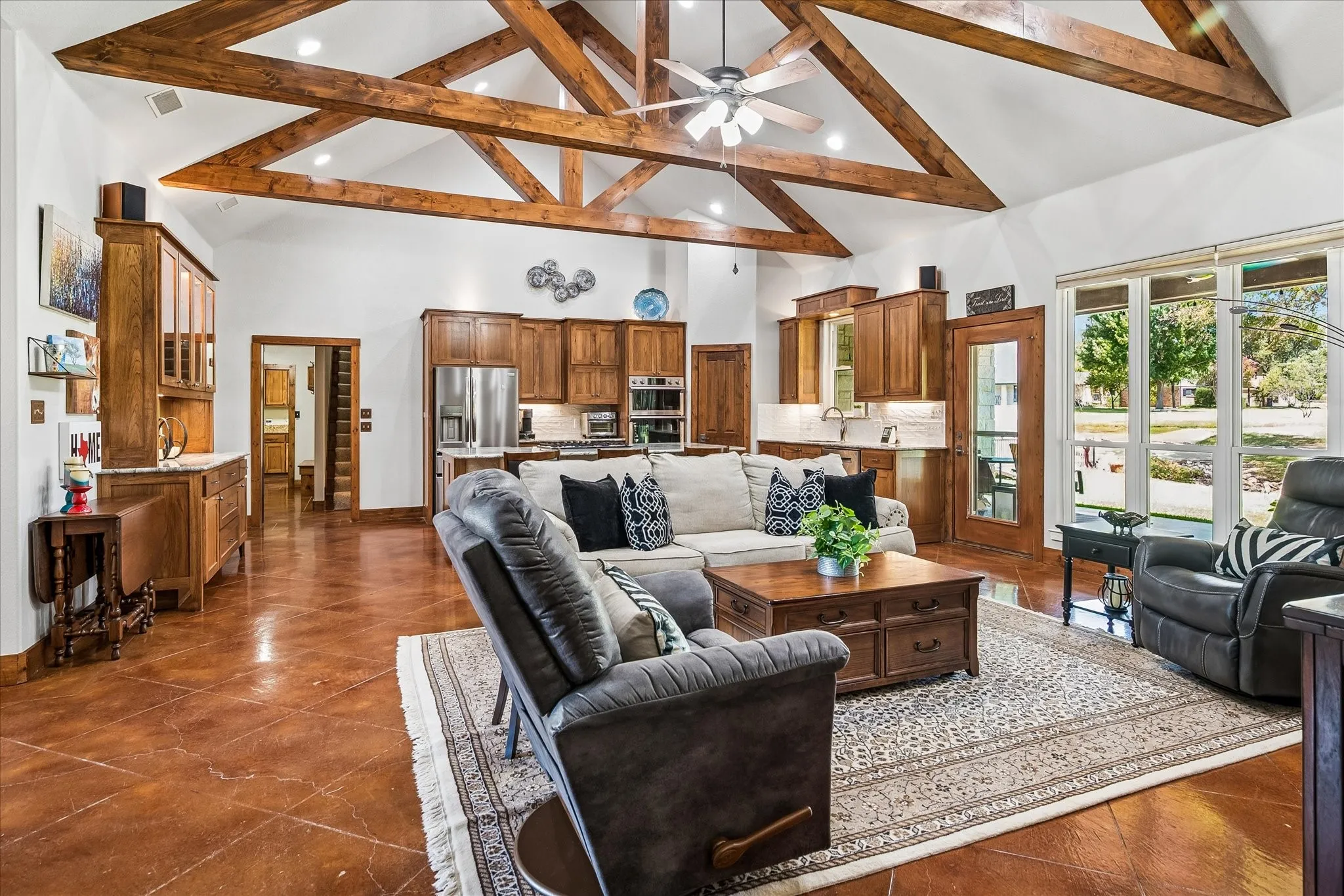 Vaulted ceiling with exposed wood beams, polished concrete flooring, built-in wooden cabinetry, stainless steel appliances, and large windows