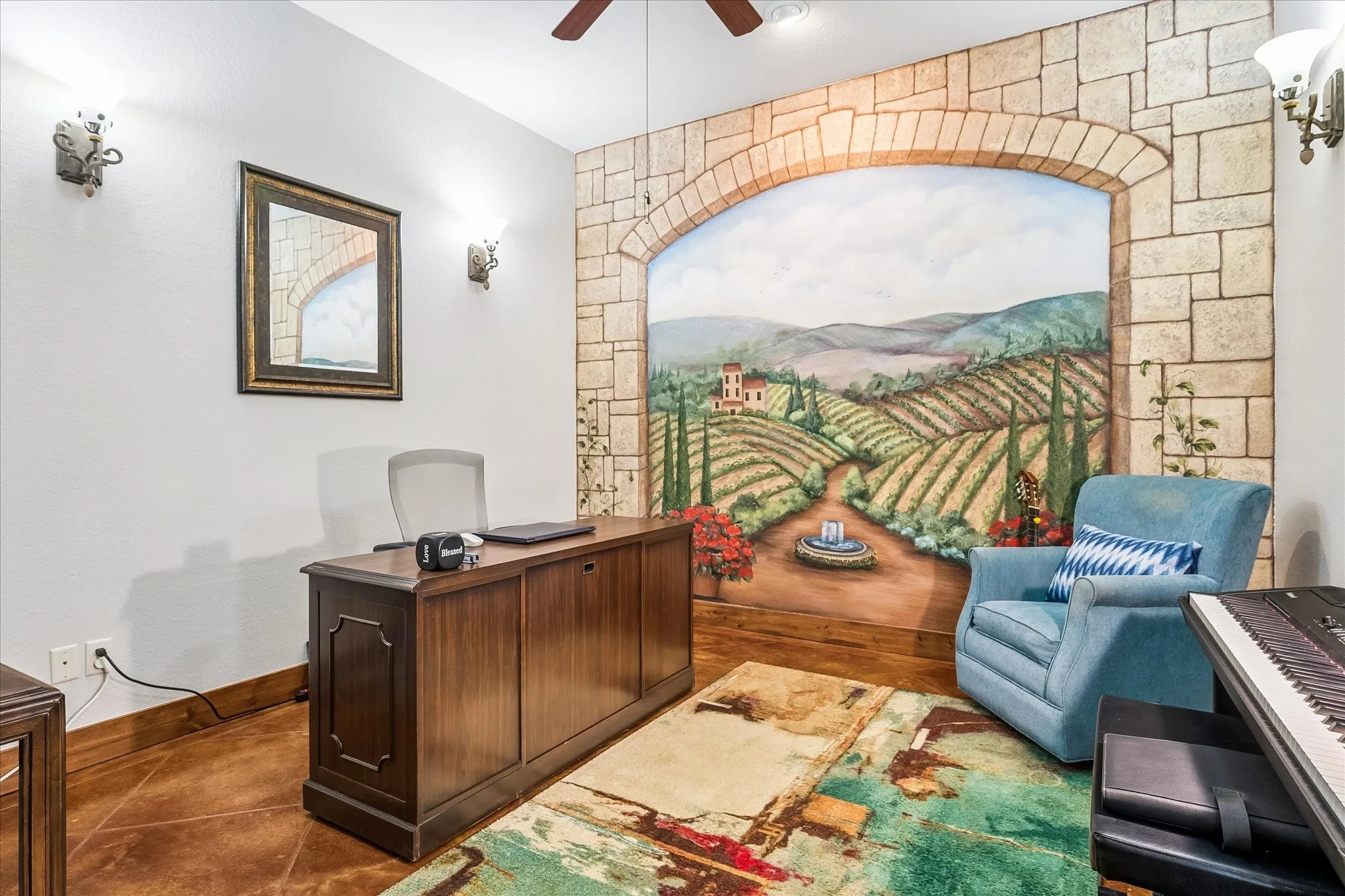 Room featuring a ceiling fan, sconce lighting, and a painted mural