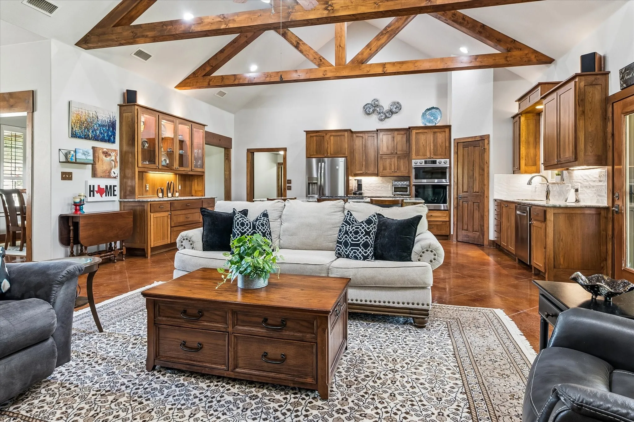 Vaulted ceiling with exposed wood beams, wood-finish flooring, built-in cabinetry, stainless steel appliances, and a white subway tile backsplash