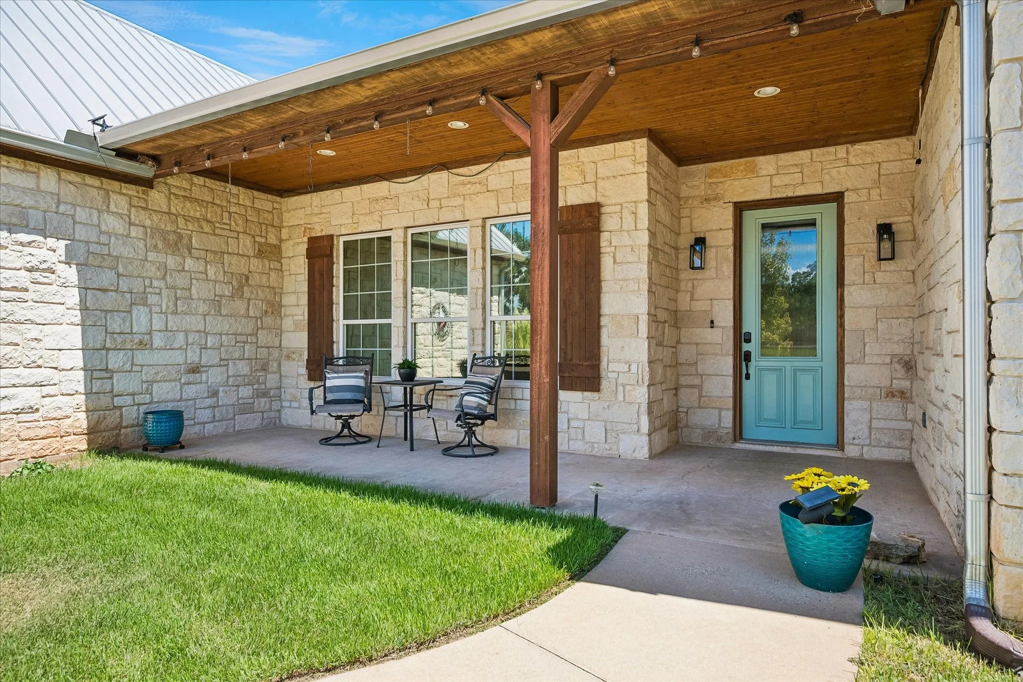 Stone exterior with a covered porch featuring a wood-finish ceiling, exposed wood beams, and recessed lighting