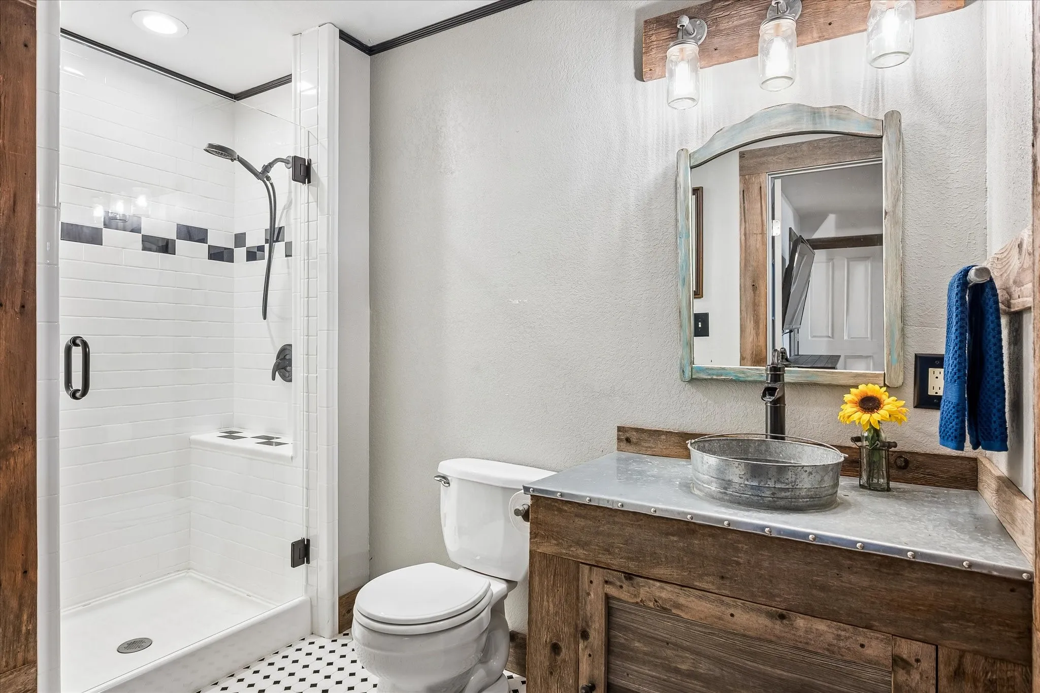 Walk-in shower with clear glass enclosure and subway tile surround, accompanied by a distressed wood-finish vanity with a vessel sink and metal countertop
