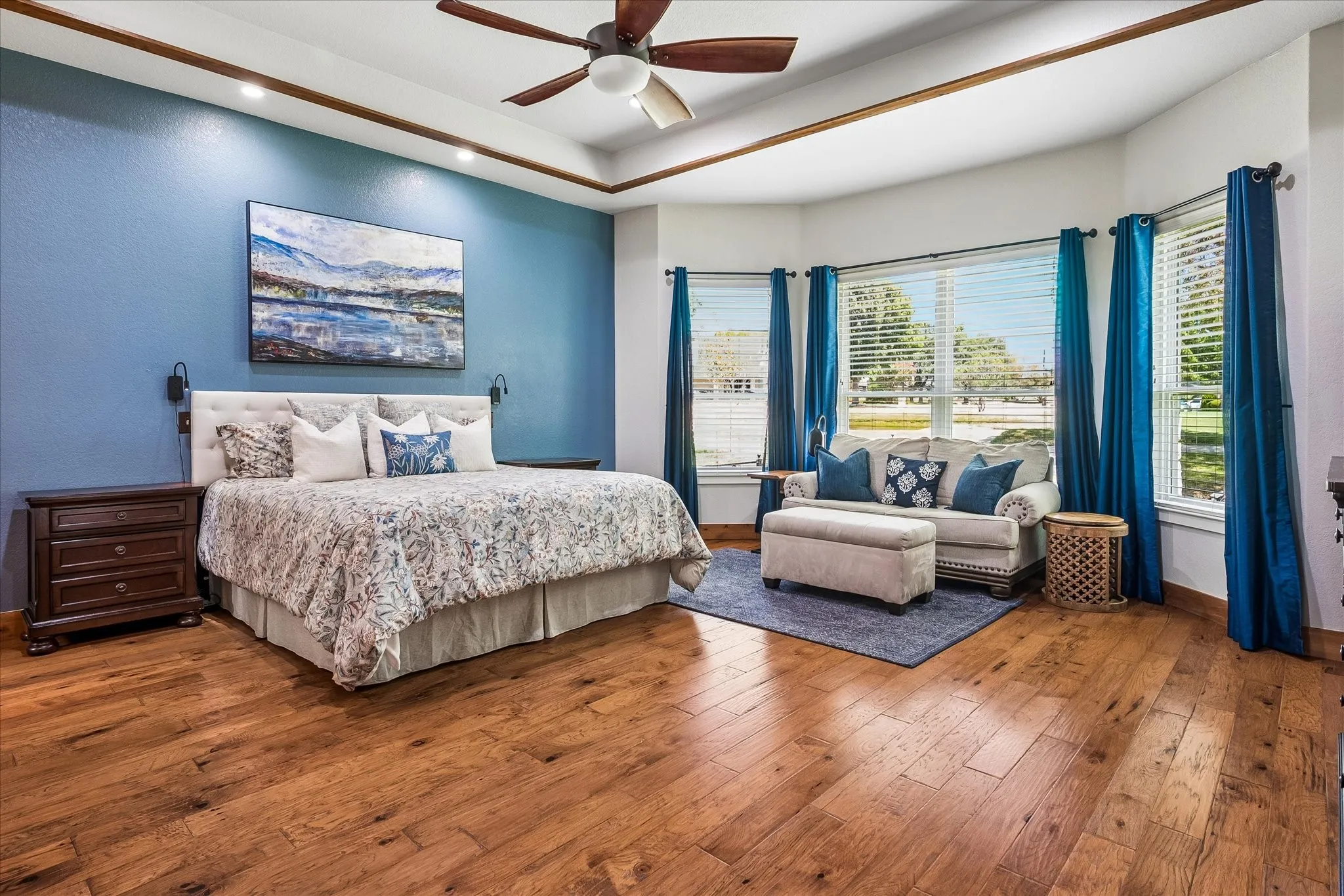 Wood-finish flooring, tray ceiling with a ceiling fan, and a curved wall with multiple windows