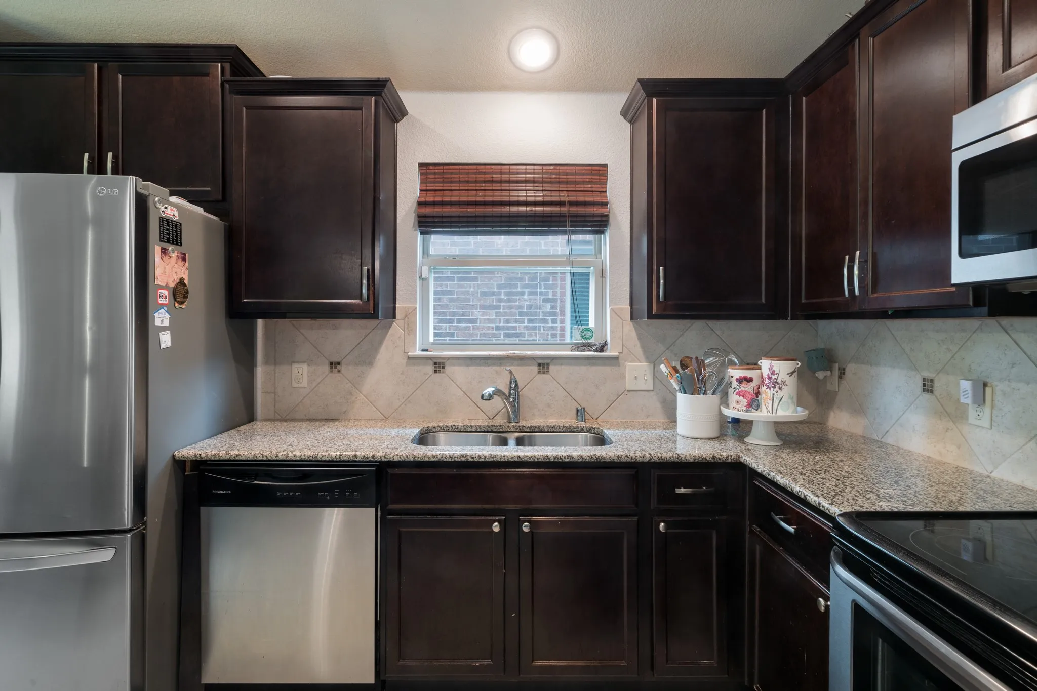 Dark wood-finish cabinetry, granite-style countertops, stainless steel appliances, tile backsplash, and a double basin sink