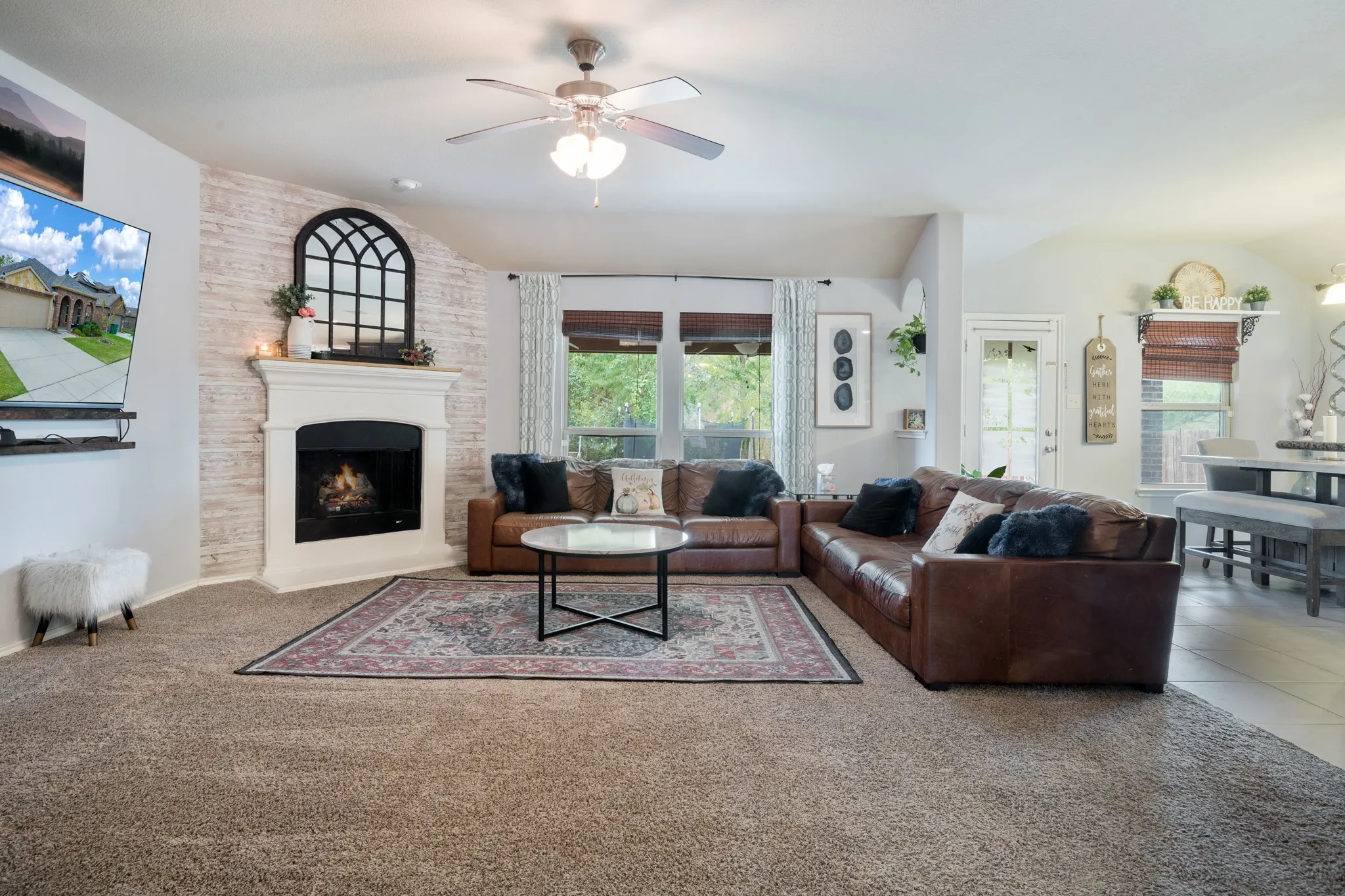 Vaulted ceiling with a ceiling fan, corner fireplace with a white mantel, textured accent wall, and multiple windows