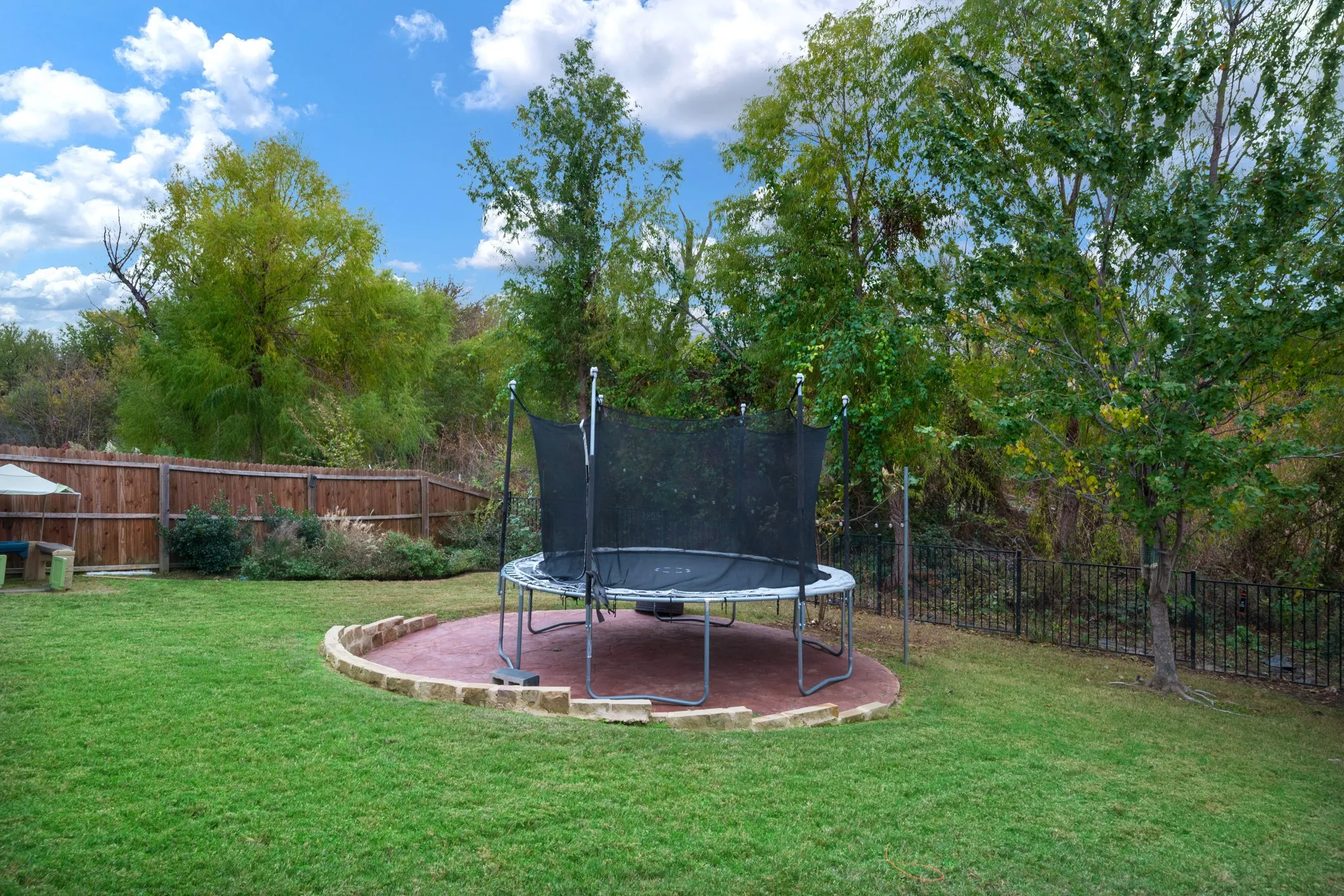 Expansive backyard with a lush lawn, privacy fencing, mature trees, and a circular paved area