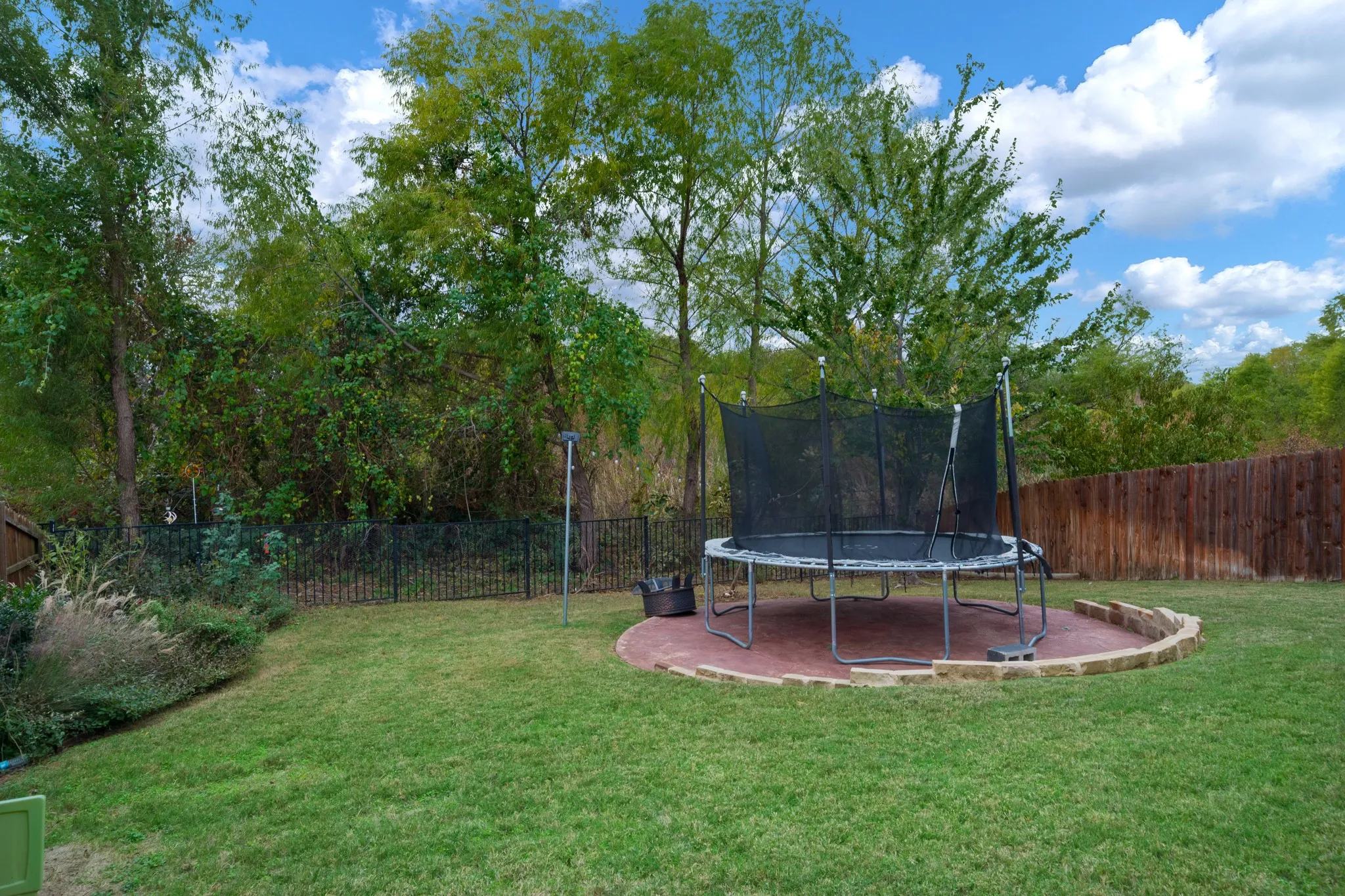 Expansive grassy area with mature trees, a wood privacy fence, and a black metal fence