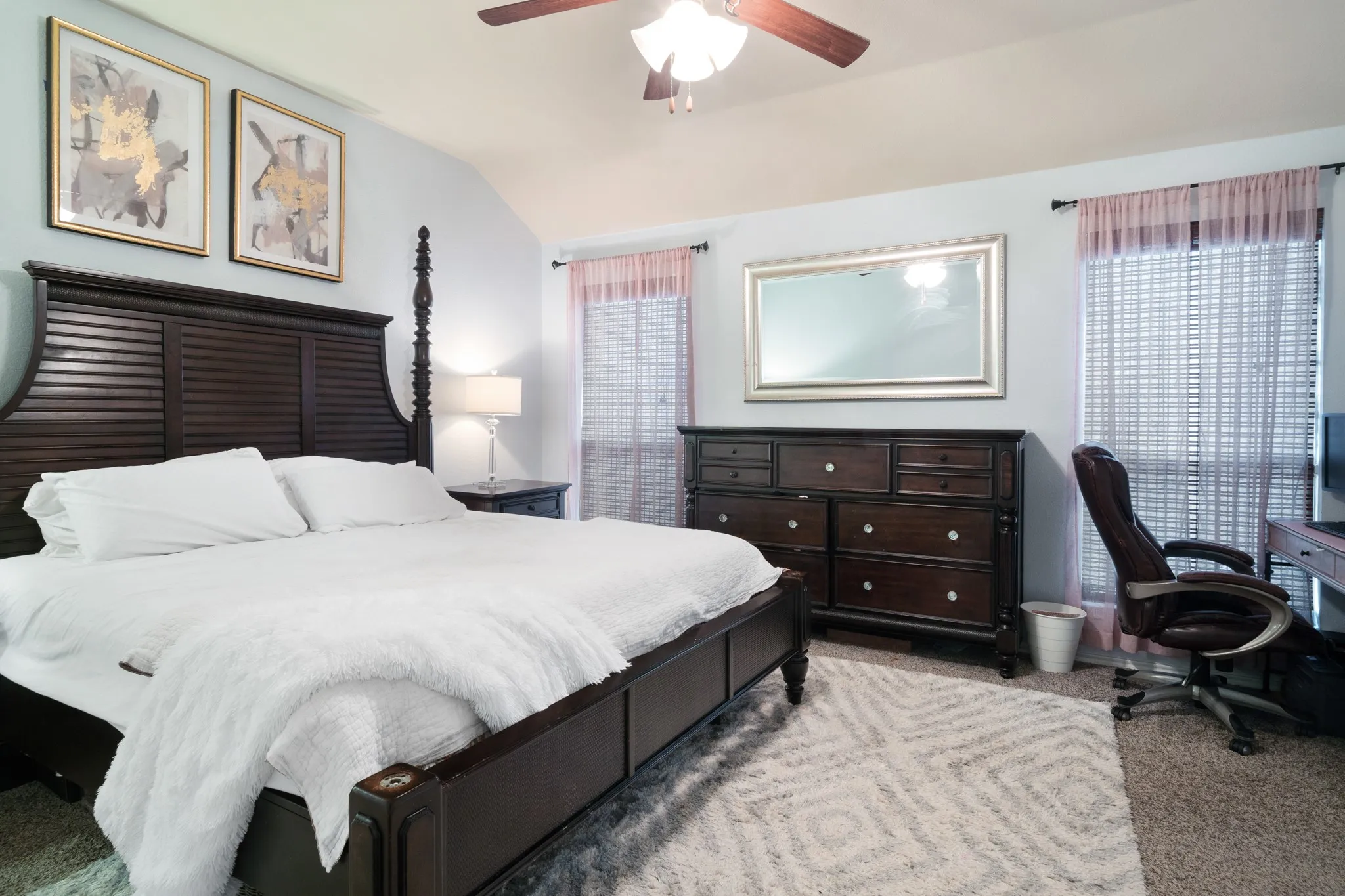 Vaulted ceiling with a ceiling fan, two windows with blinds, and light-colored walls