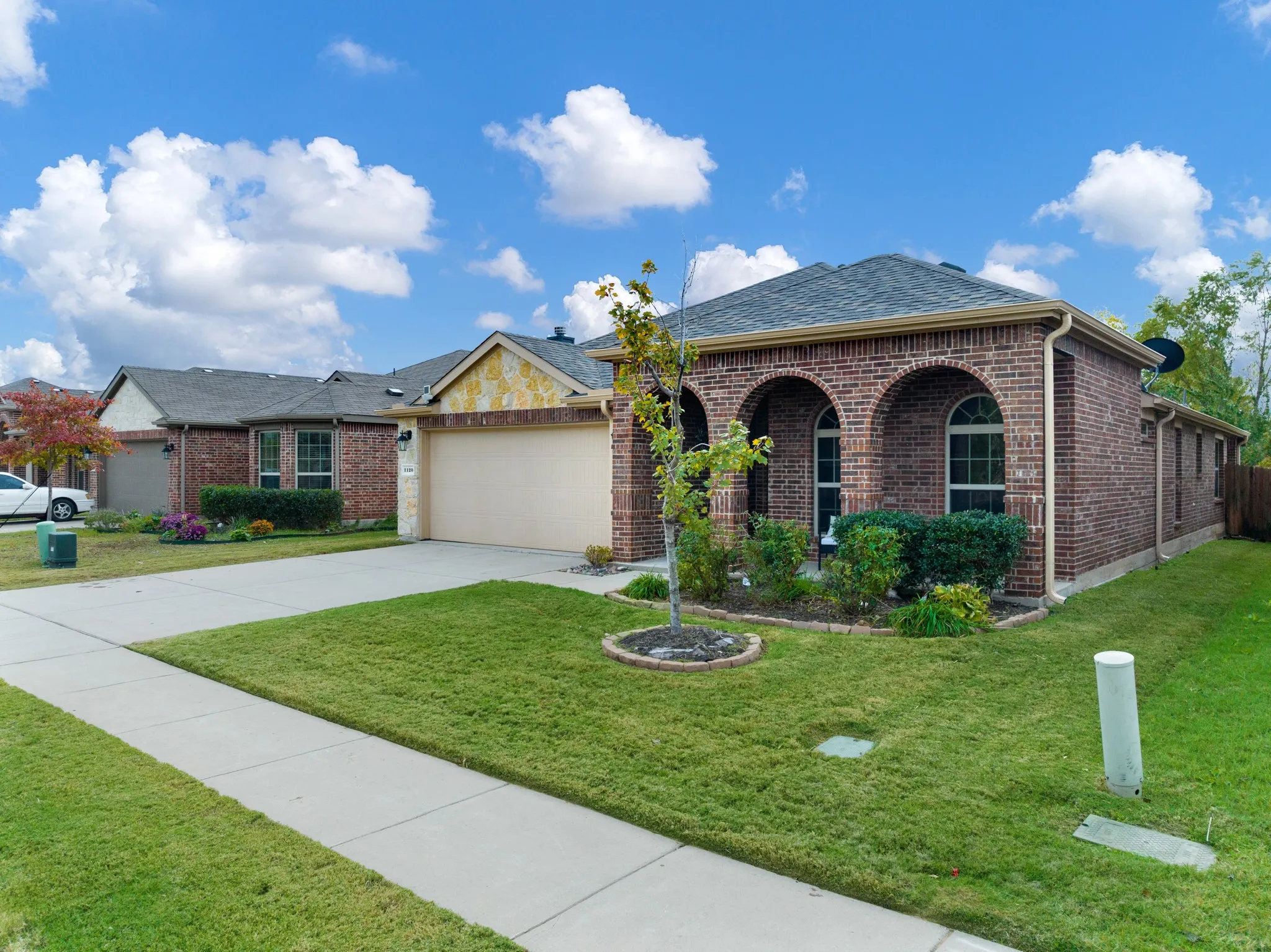 Brick exterior with arched windows, attached garage, and mature landscaping