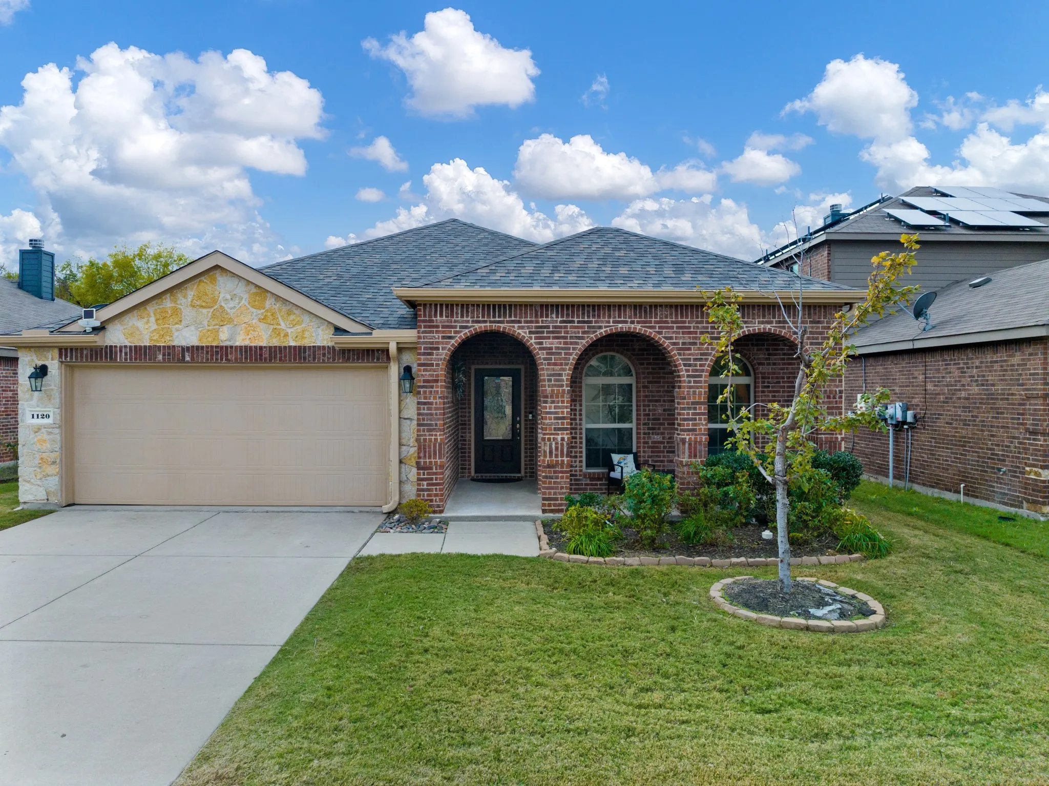 Brick exterior with stone accents, arched entryway, attached garage, concrete driveway, and front landscaping