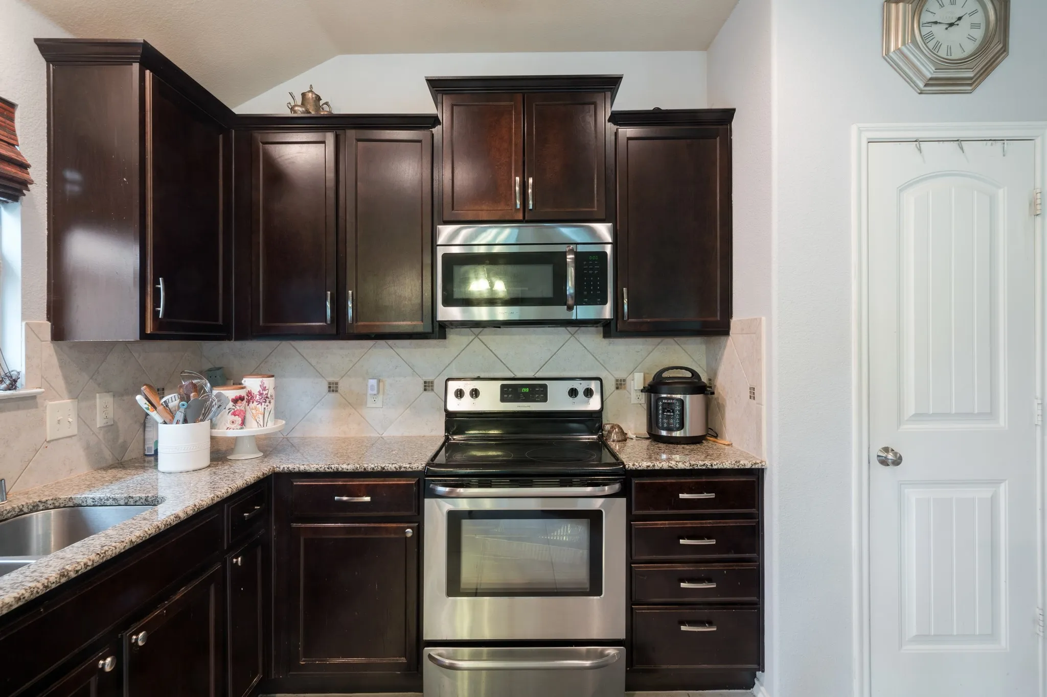 Dark wood-finish cabinetry, stainless steel appliances, granite countertops, and a tiled backsplash