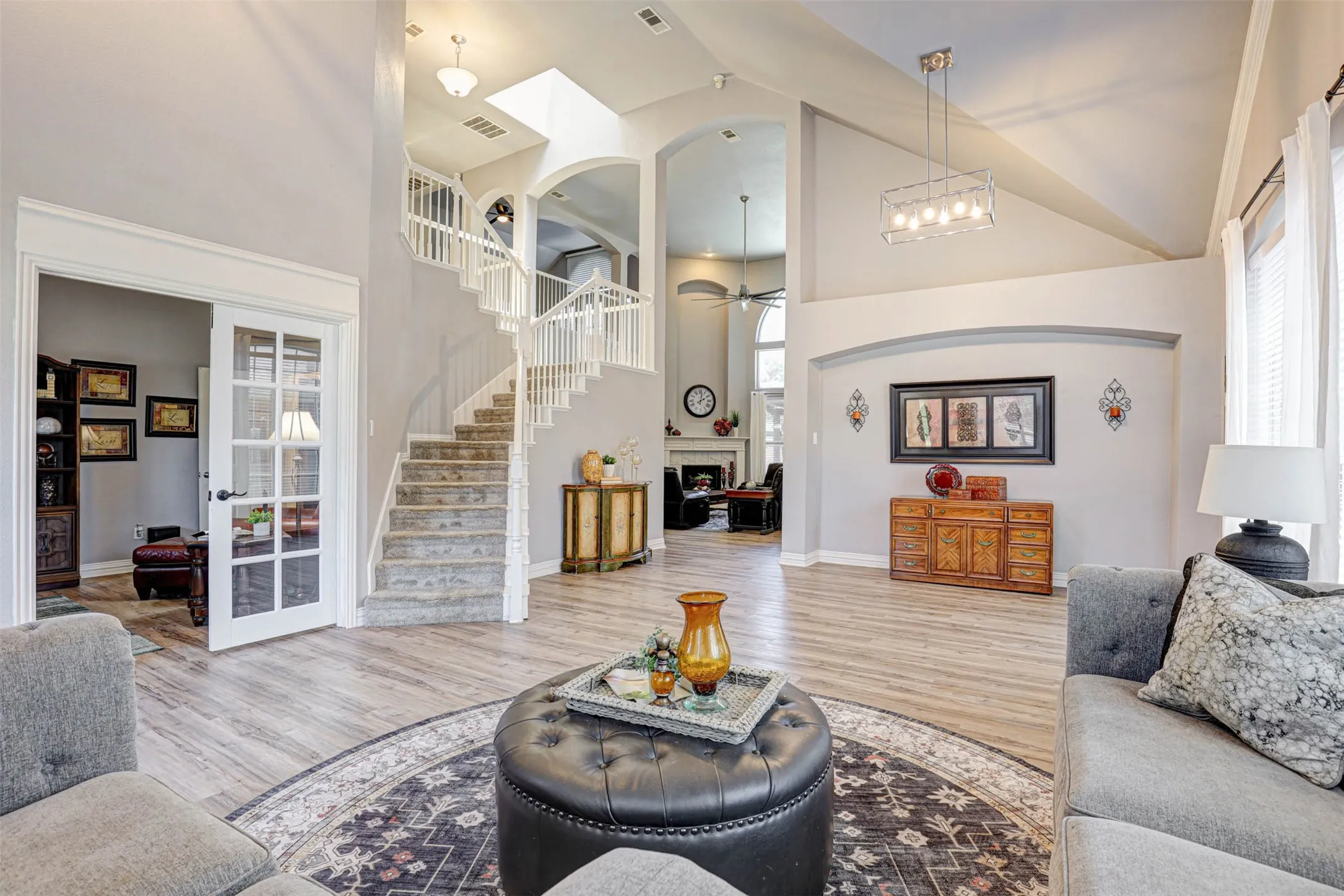 The open floorplan connects the living room seamlessly to the dining area, office, and family room, with beautiful ceiling treatments and a staircase as the centerpiece.