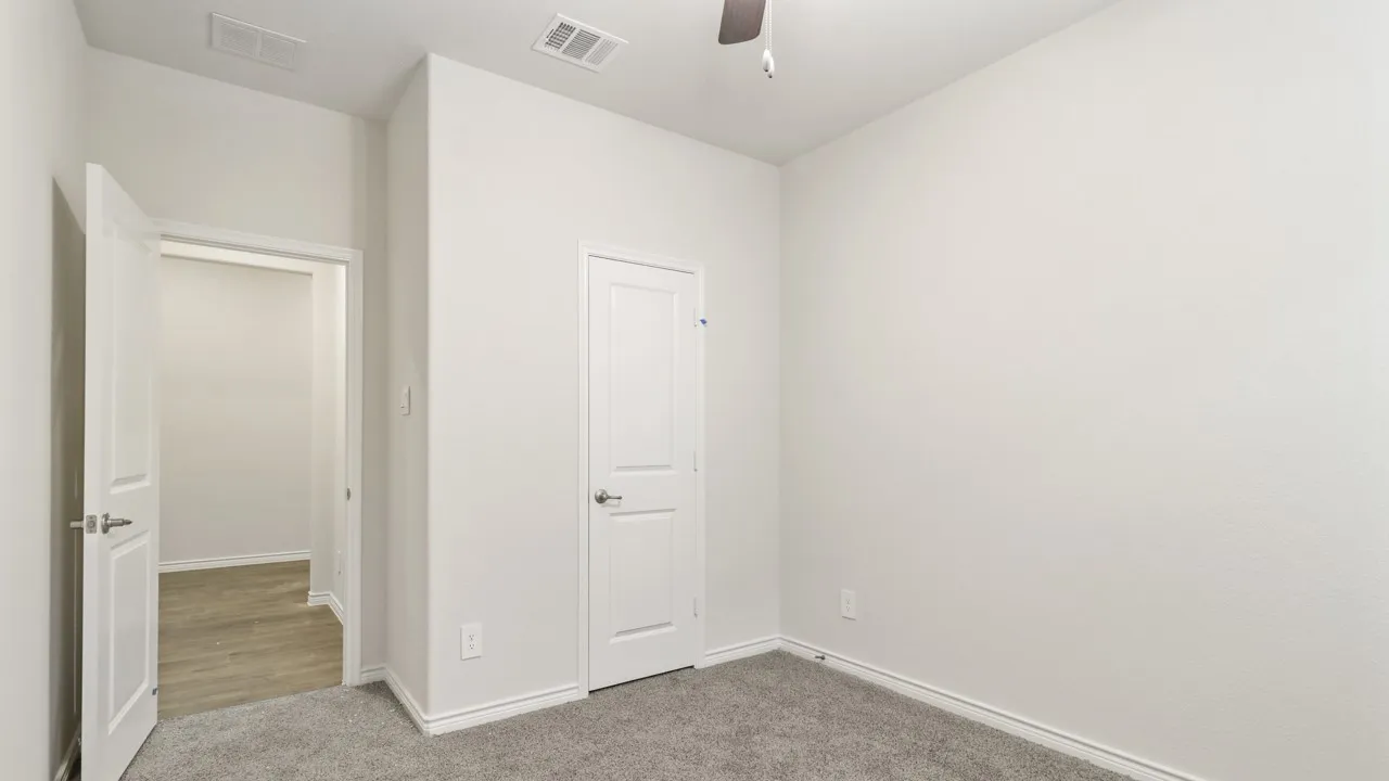 Textured walls with neutral paint, gray carpeting, a white paneled door, and a ceiling fan