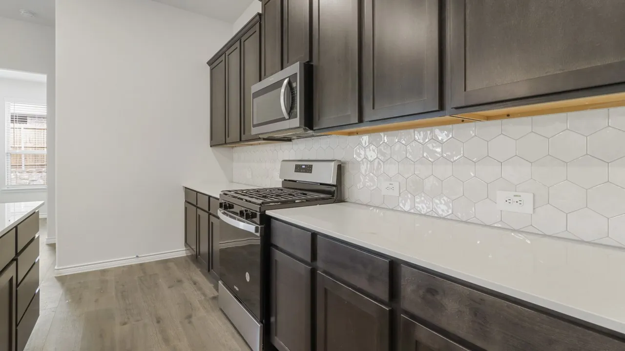 Kitchen featuring dark wood-finish cabinetry, light-toned countertops, a geometric tile backsplash, stainless steel appliances, and wood-finish flooring