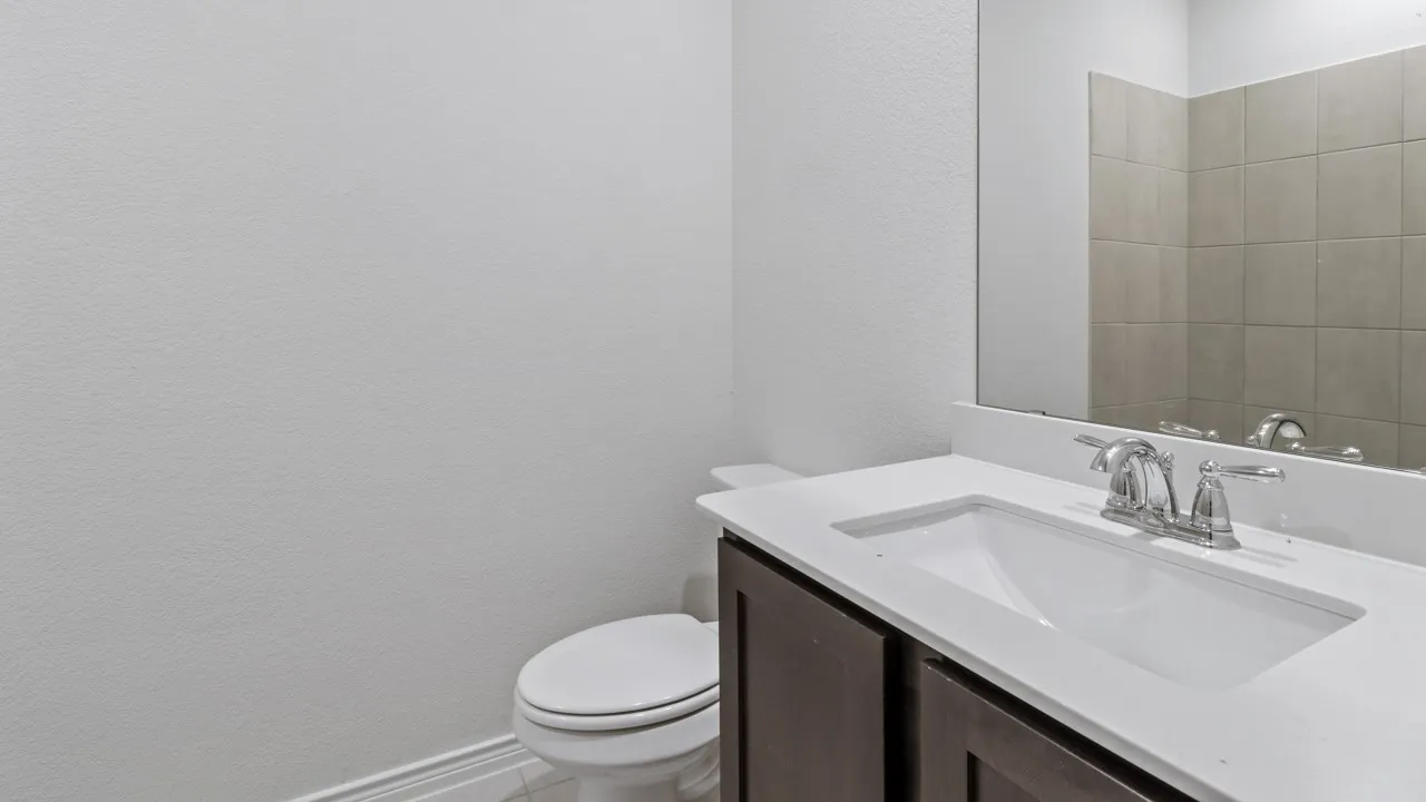 Vanity with white countertop and integrated sink, chrome faucet, dark wood-finish cabinetry, and tiled wall