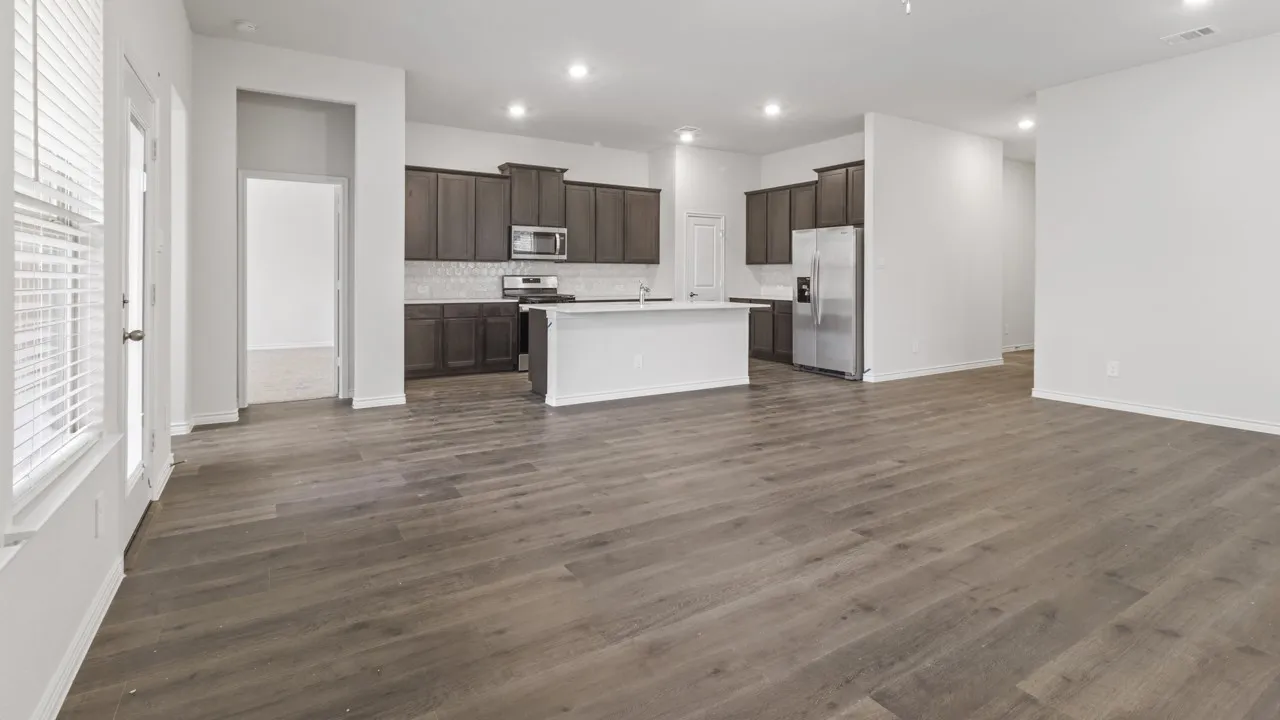 Open-concept living and kitchen area featuring wood-finish flooring throughout, dark cabinetry with stainless steel appliances, a white quartz island with seating, recessed lighting, and abundant natural light from multiple windows
