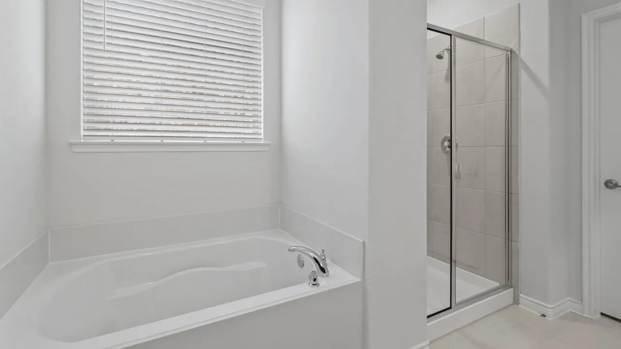 Soaking tub with chrome fixtures, adjacent glass-enclosed shower, and tile flooring