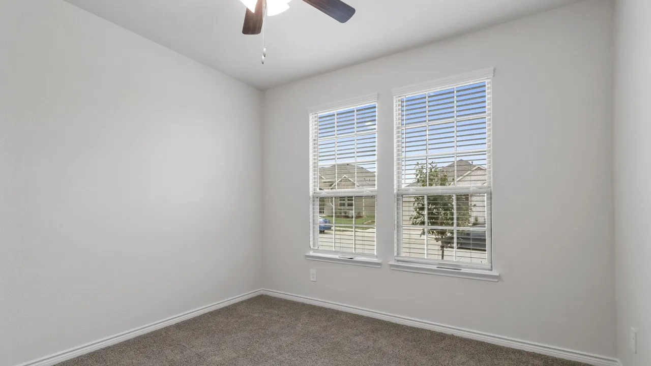 Two windows with blinds, gray carpeting, neutral wall color, and a ceiling fan with light fixture