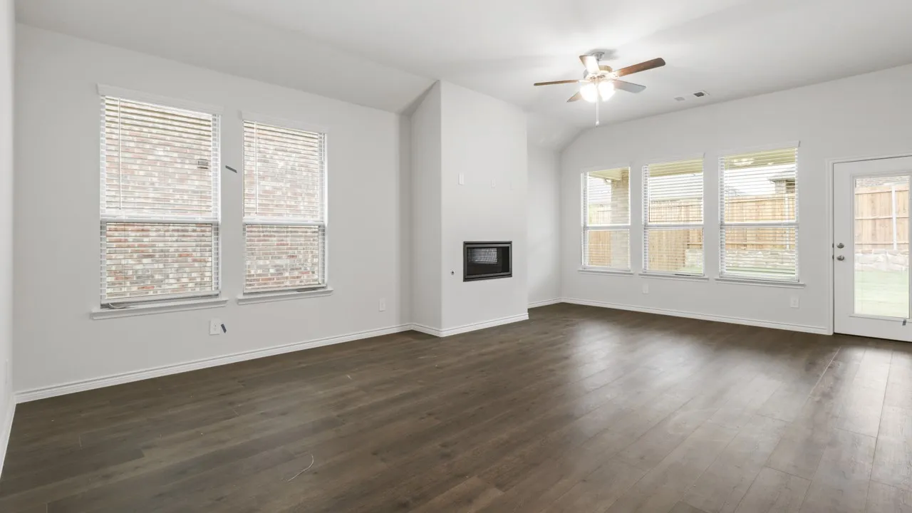 Spacious living area featuring wood-finish flooring, a ceiling fan, a built-in fireplace, and multiple windows