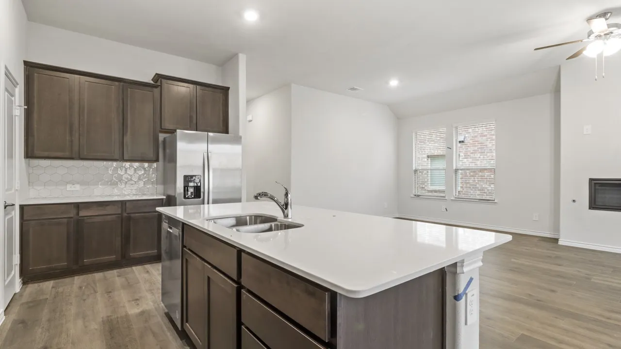 Spacious kitchen featuring an expansive island with an undermount sink, stainless steel appliances, dark wood cabinetry, and a patterned tile backsplash