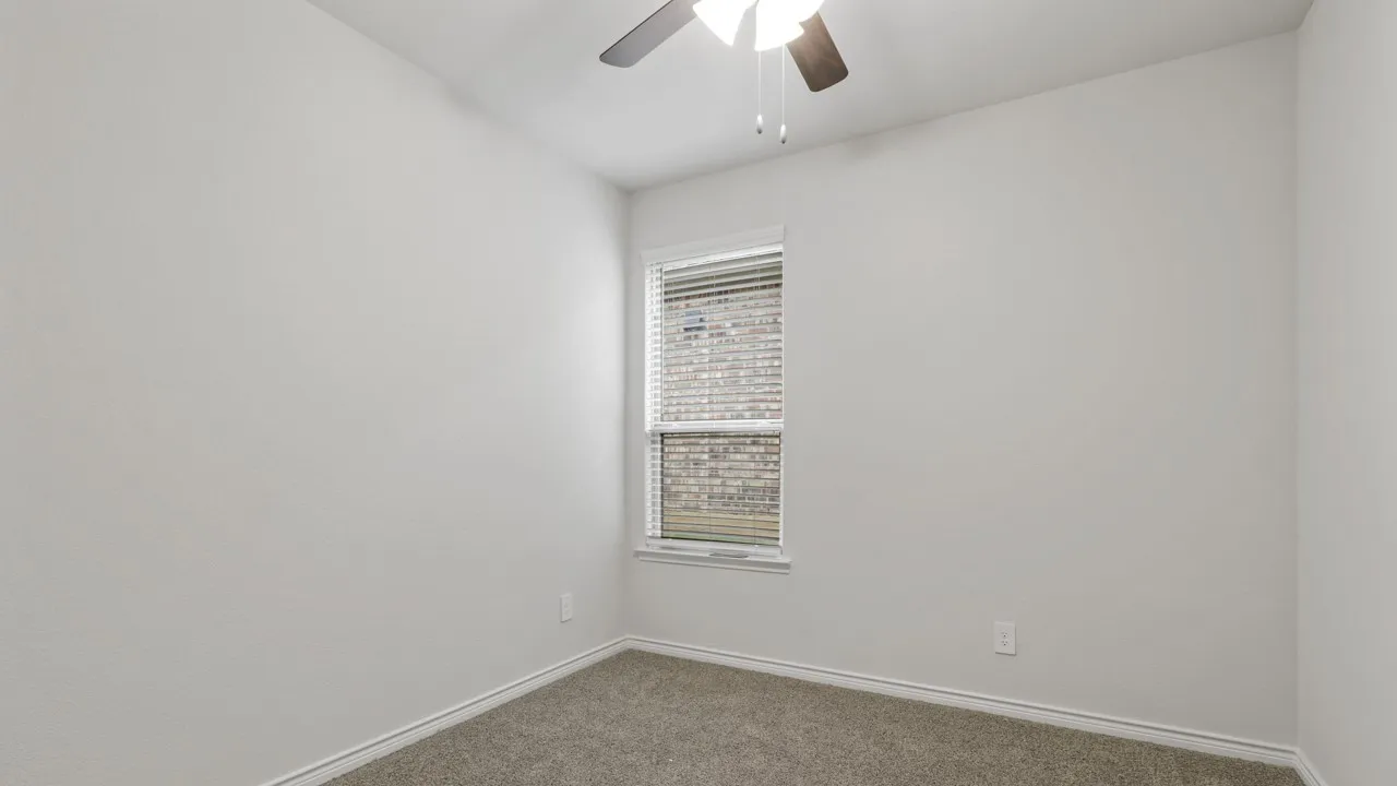 Neutral wall paint, carpeted flooring, a window with horizontal blinds, and a ceiling fan with integrated lighting