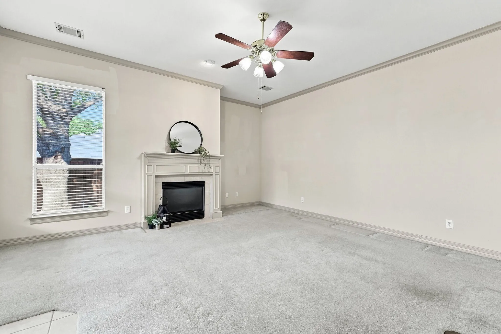 Carpeted room featuring a fireplace with a decorative mantel, a window with blinds, and a ceiling fan with light fixture