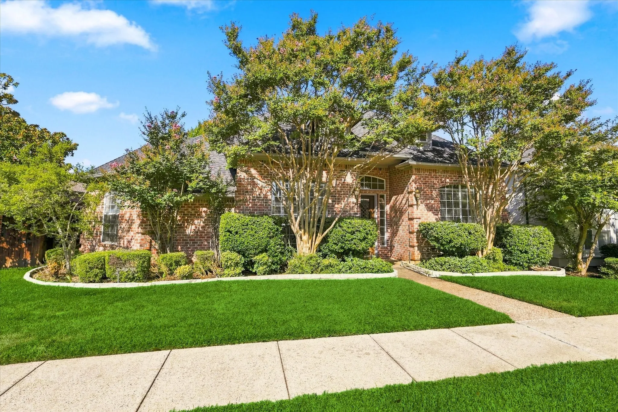 Brick facade residence with a gabled roof, mature landscaping, sidewalk, and a concrete pathway