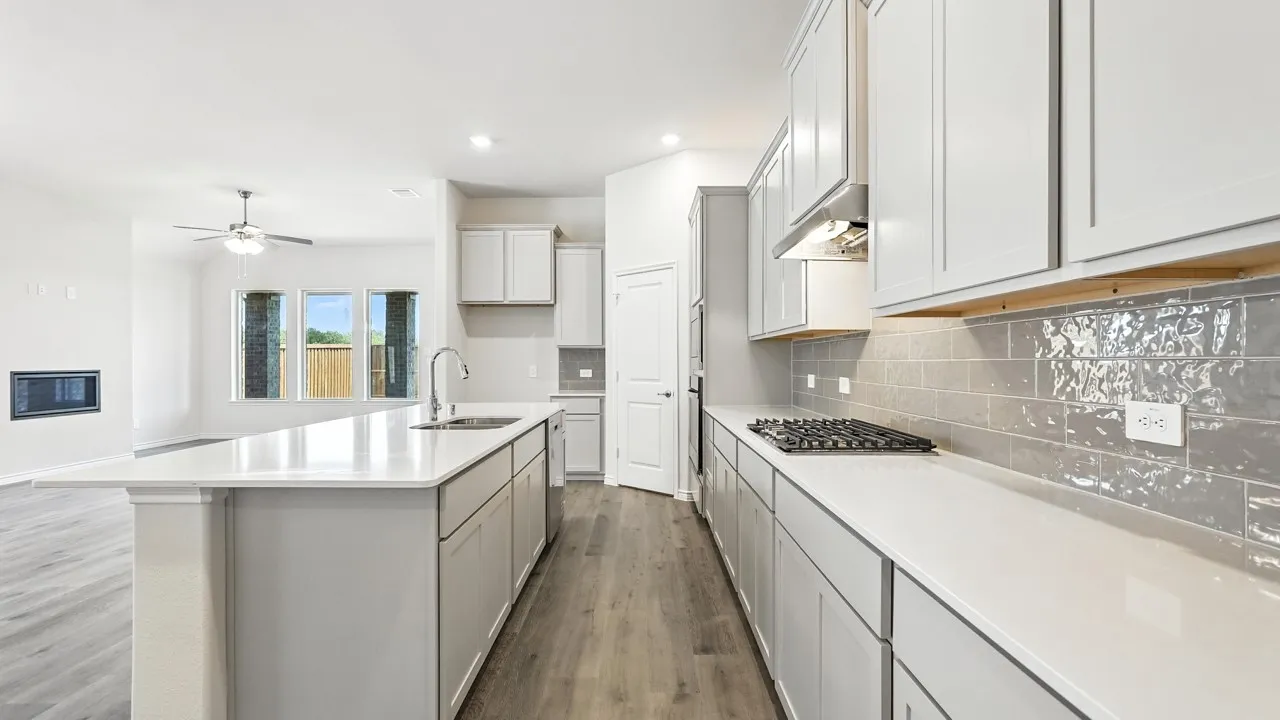 Kitchen with a gas cooktop, subway tile backsplash, light grey cabinetry, and a center island with a sink and white countertop
