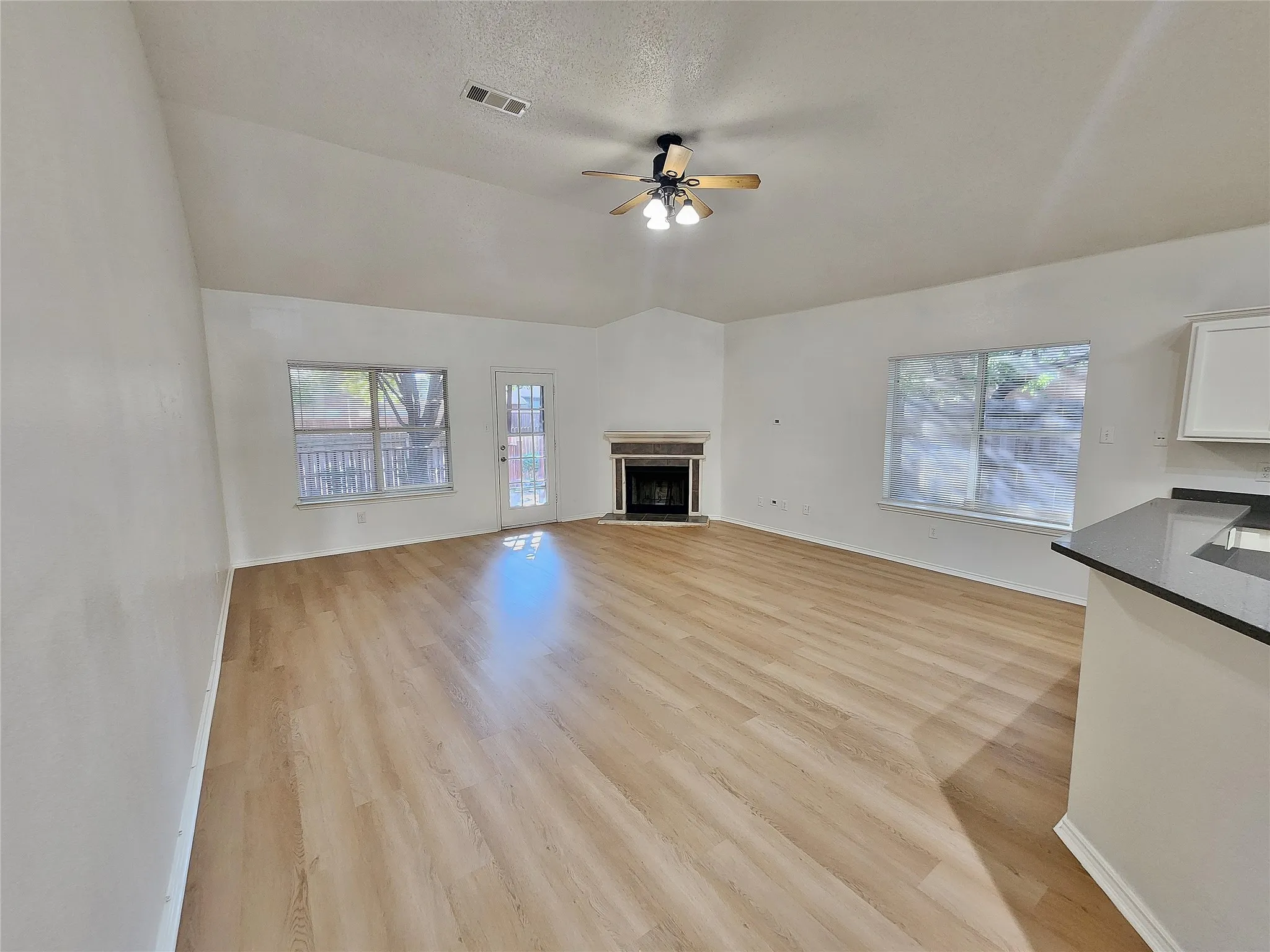 Vaulted ceiling, ceiling fan with integrated lighting, wood-finish flooring, fireplace with stone surround, and a breakfast bar with a dark countertop