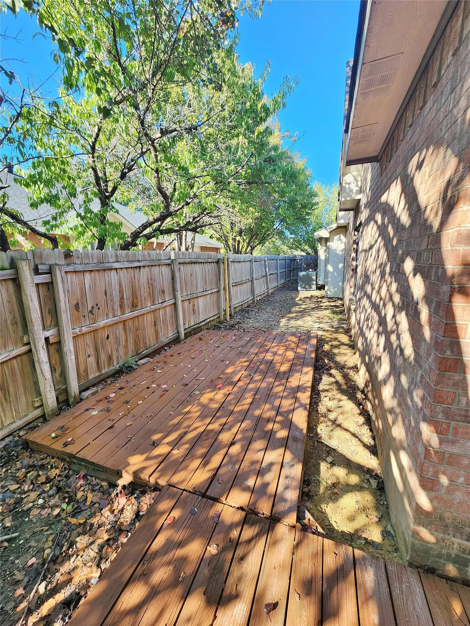 Wood plank walkway, brick exterior, wood privacy fence, mature trees, clear sky