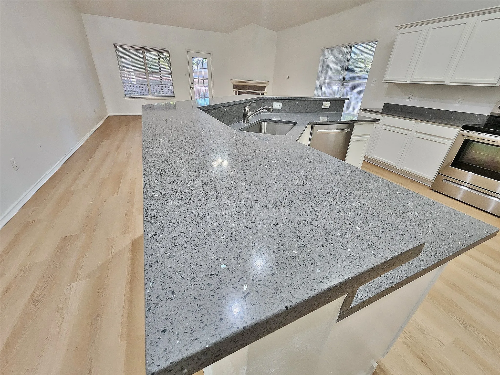 Spacious kitchen featuring light wood-finish flooring, white cabinetry, and speckled grey countertops