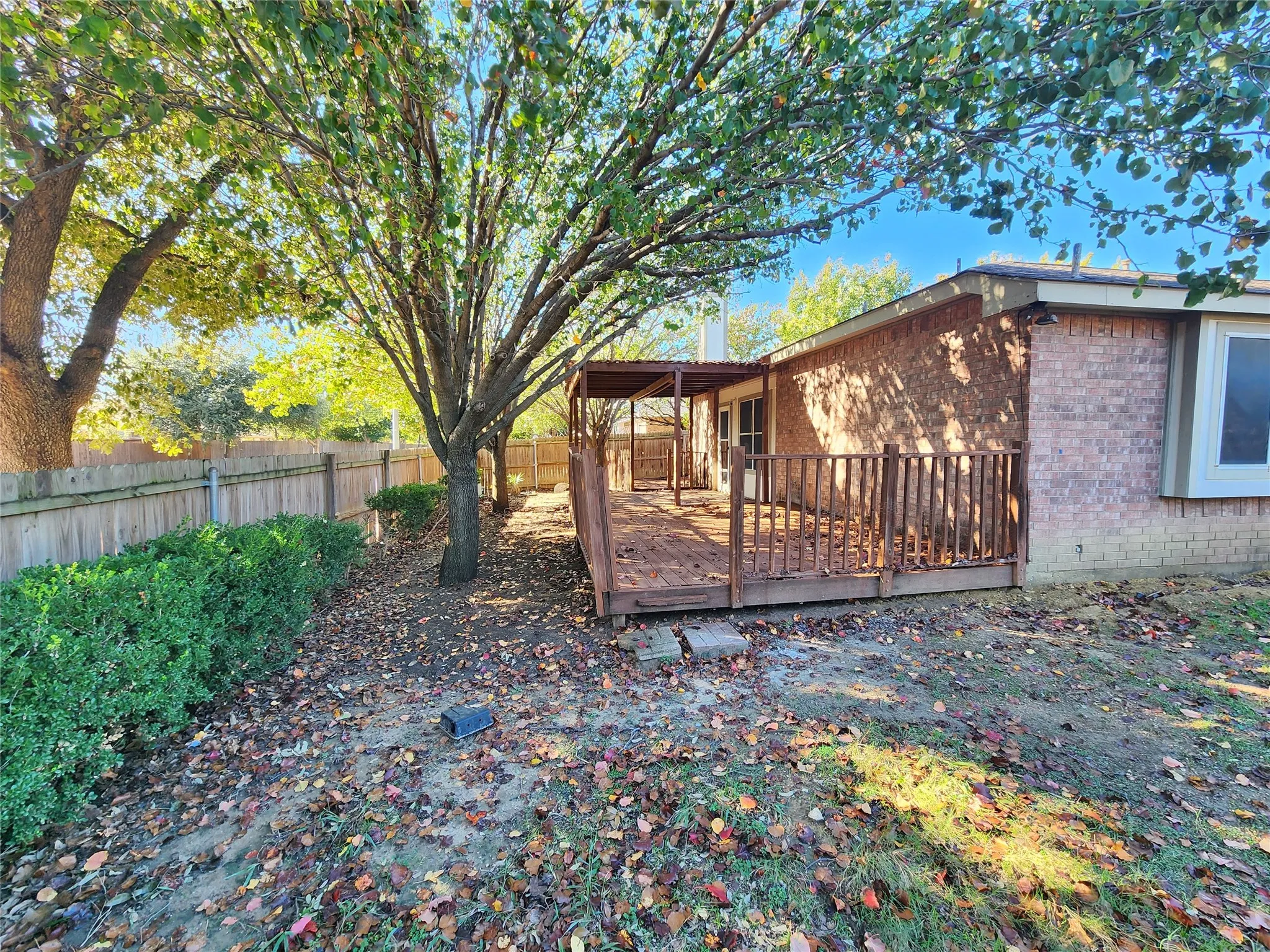 Expansive wood deck with a covered pergola, brick exterior, and established trees